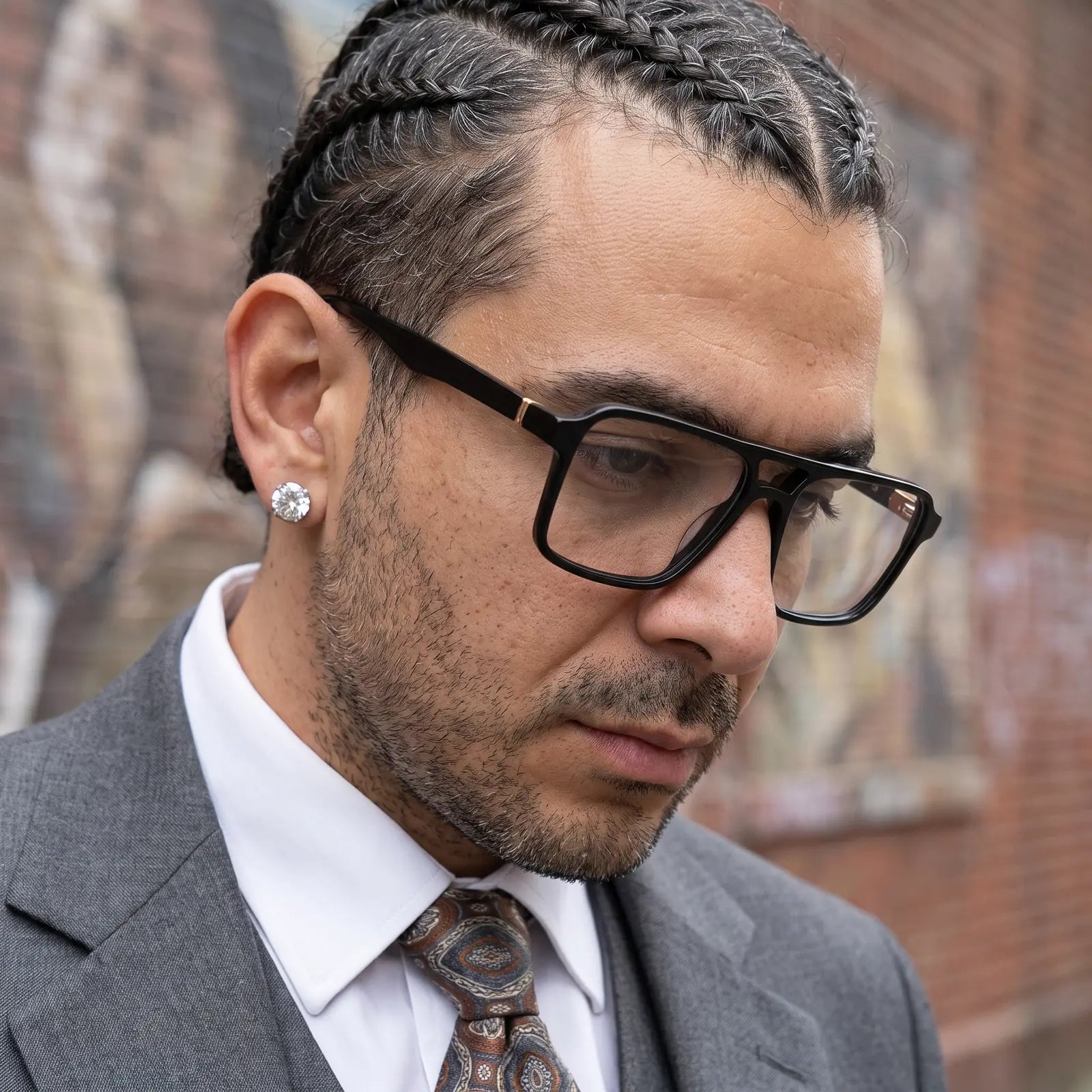 Fiore 1039 eyeglasses in black, worn by a model – campaign portrait, pensive portrait against a painted brick mural