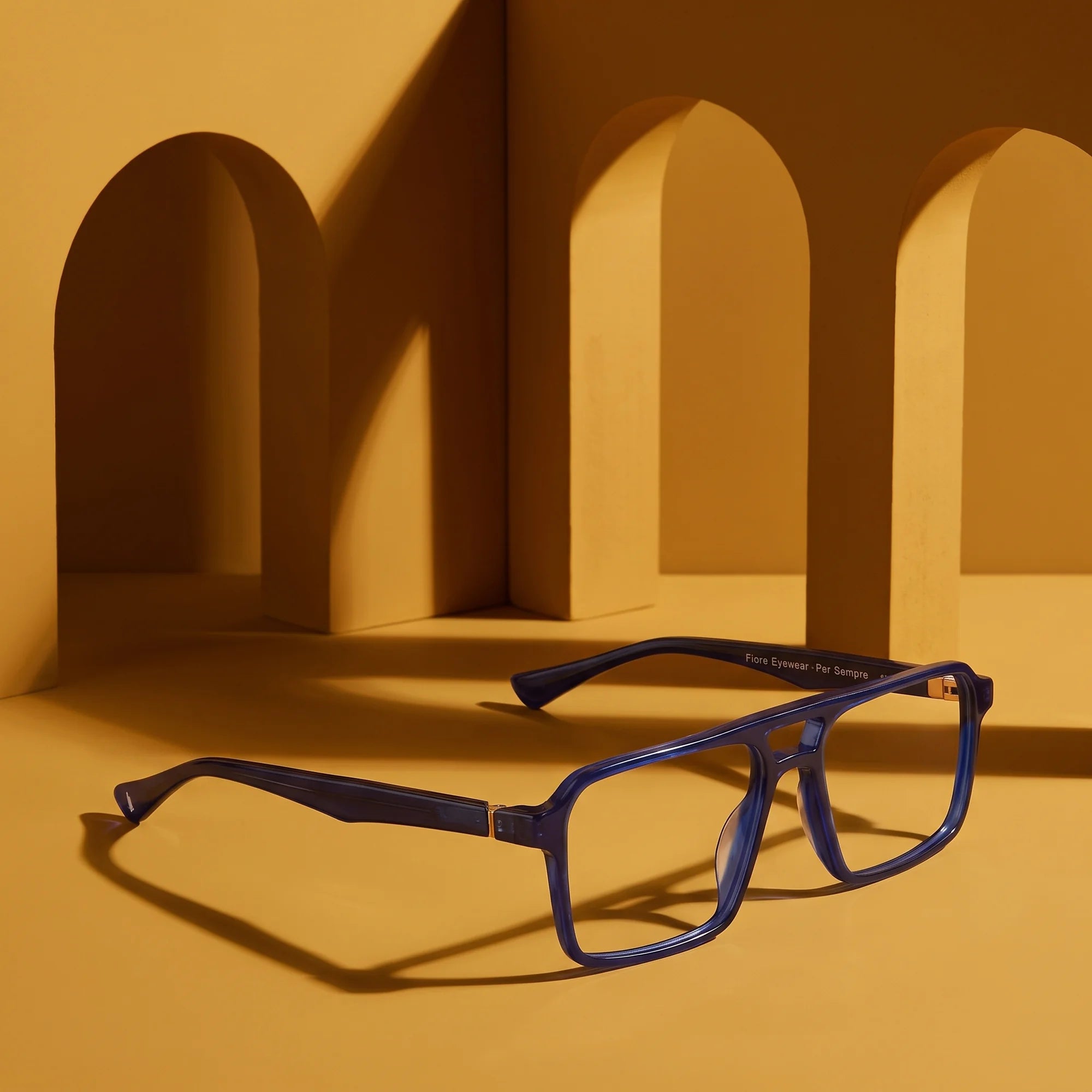 Fiore 1039 eyeglasses in blue – displayed on a mustard ochre podium among arches