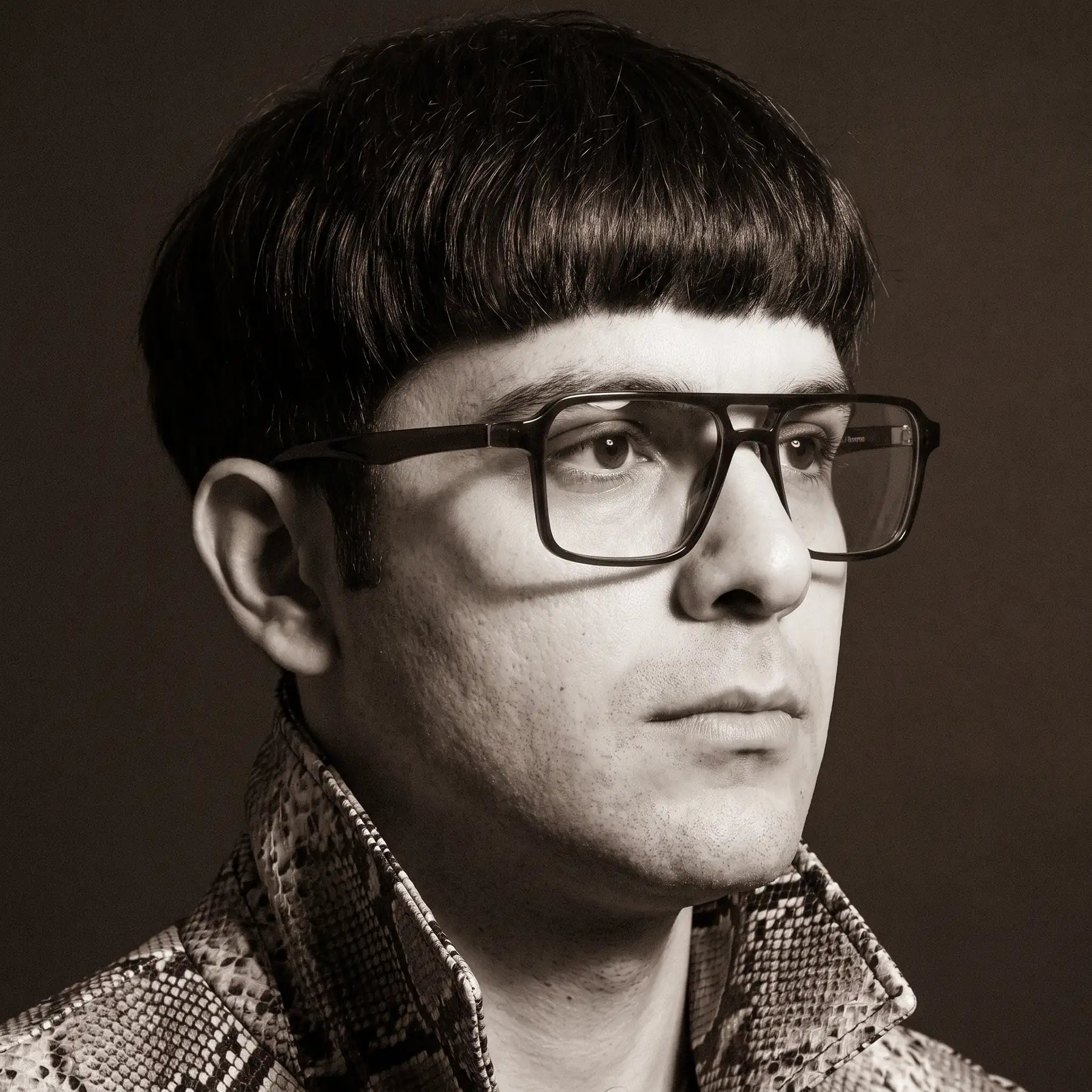 Fiore 1039 eyeglasses in brown, worn by a model – campaign portrait, monochrome studio portrait, red graphic accents