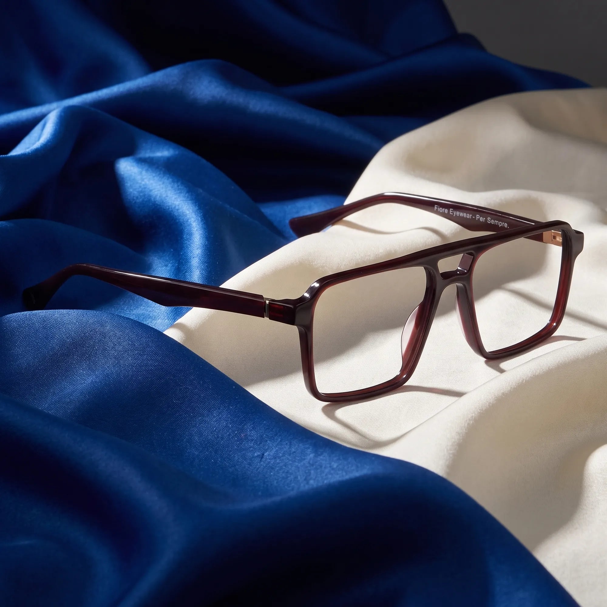 Fiore 1039 eyeglasses in brown – resting on draped cobalt and ivory silk