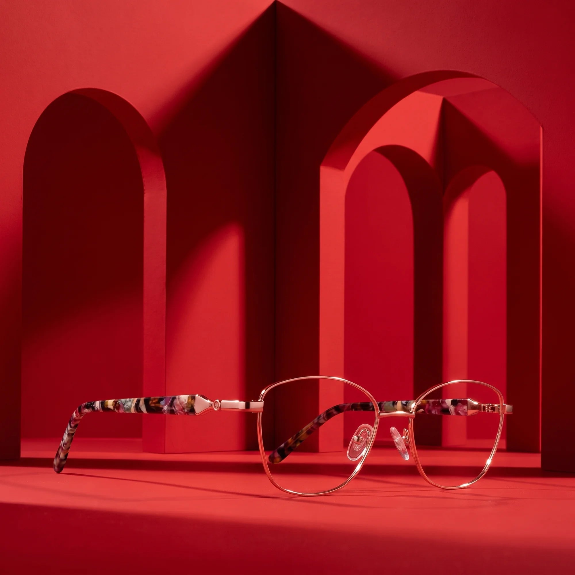 Fiore 2208 eyeglasses in brown gold – displayed on a vivid red podium among arches