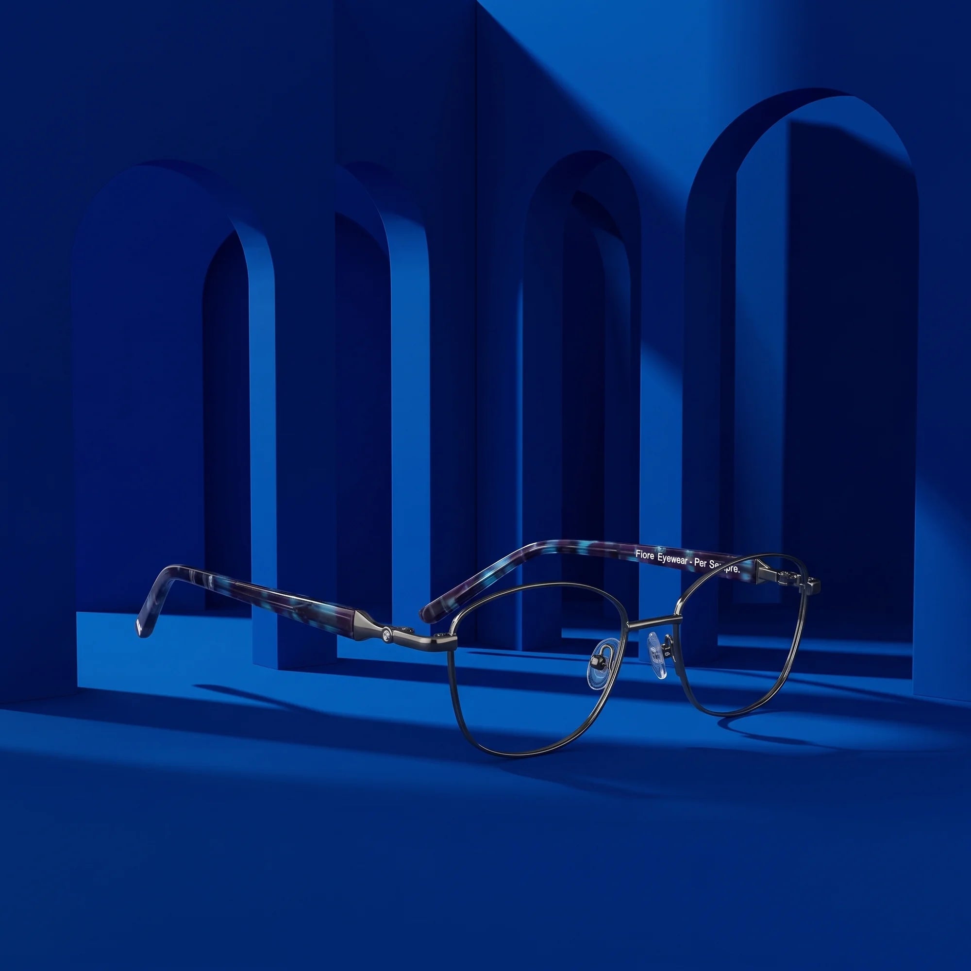 Fiore 2208 eyeglasses in gun blue – displayed on a cobalt podium among arches