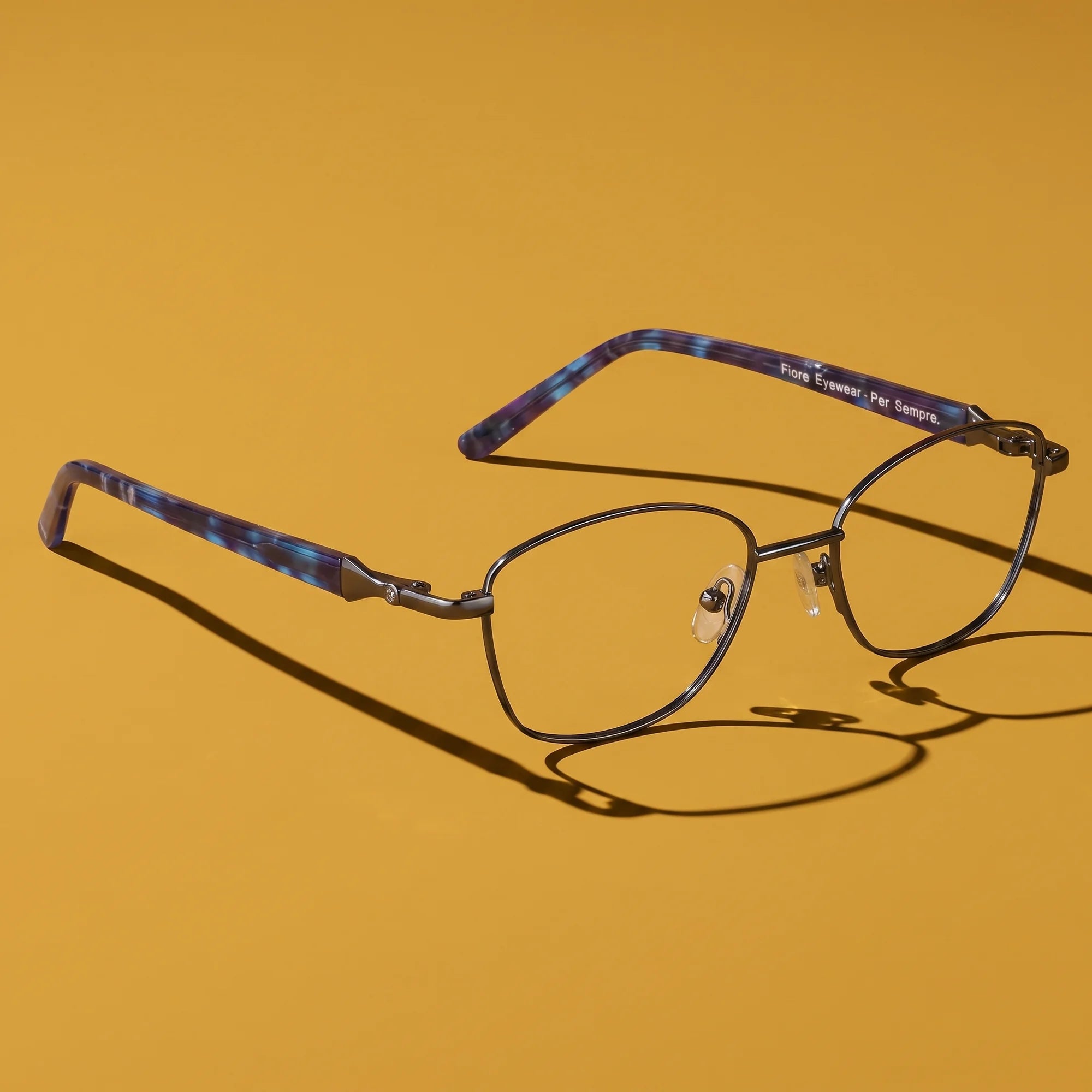 Fiore 2208 eyeglasses in gun blue – hero still life against a deep mustard ochre backdrop