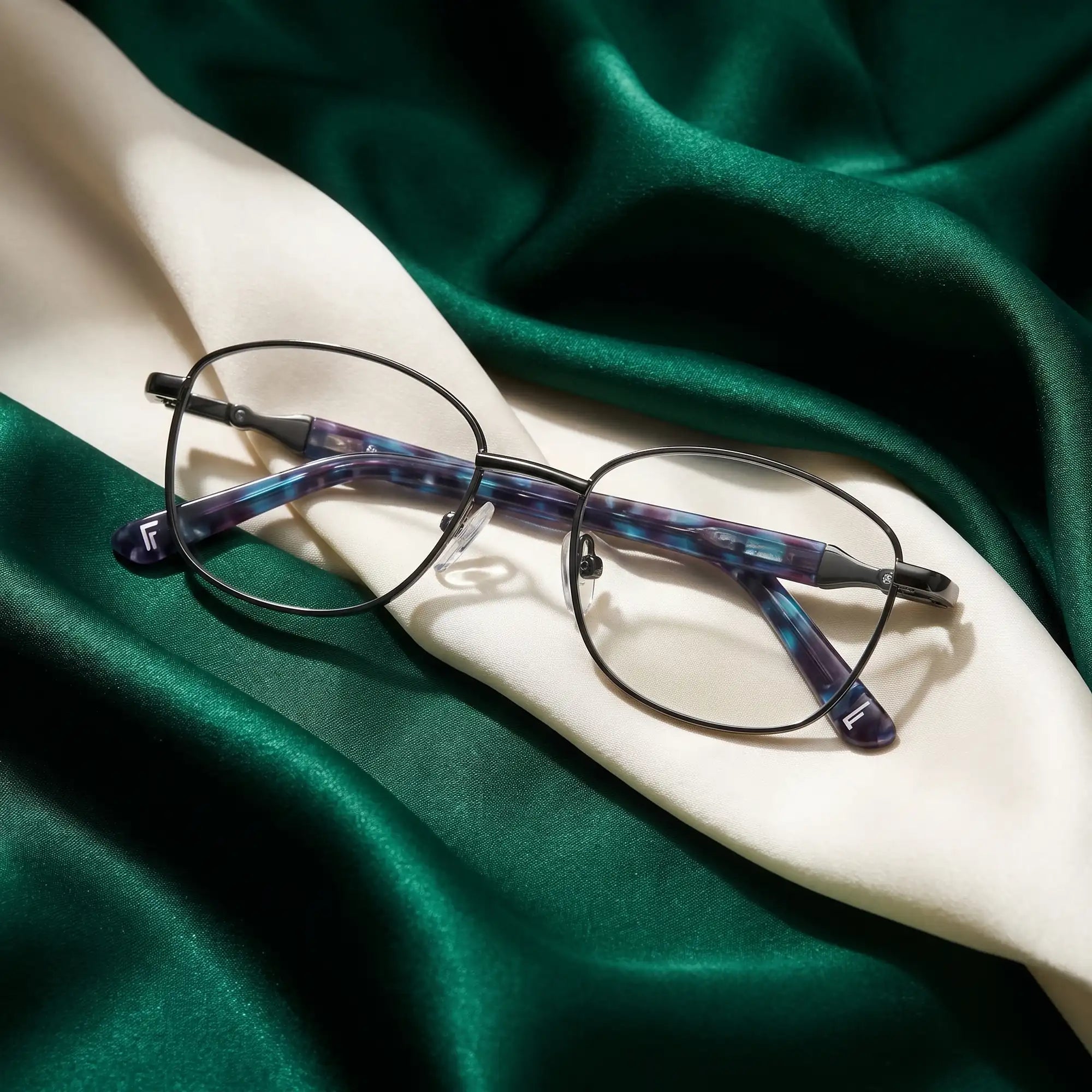 Fiore 2208 eyeglasses in gun blue – resting on draped emerald and ivory silk