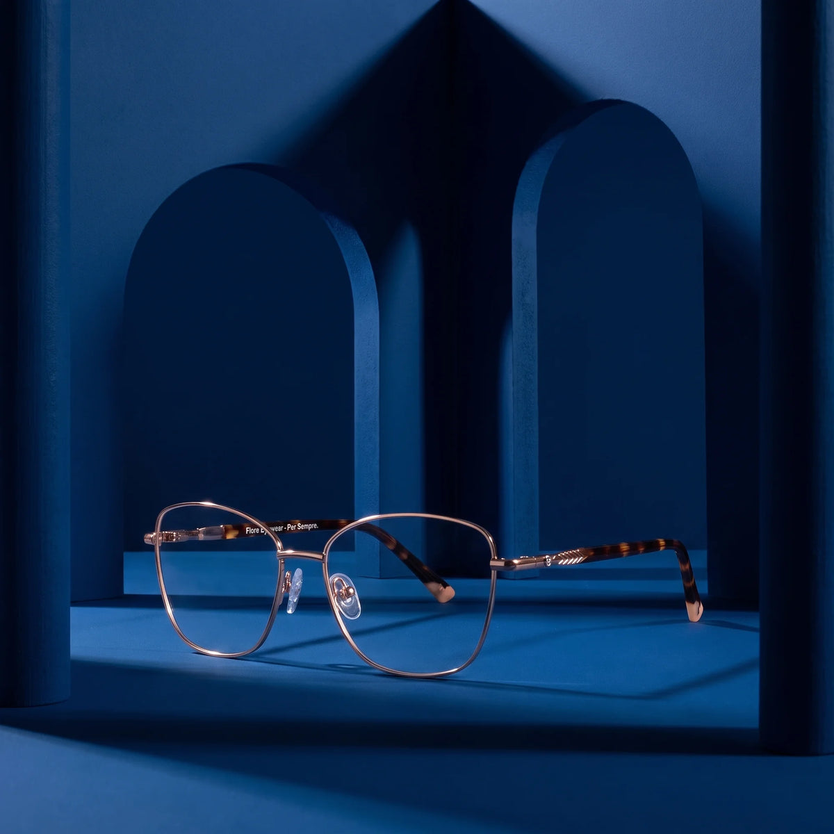 Fiore 2210 eyeglasses in gold pink – displayed on a midnight blue podium among arches