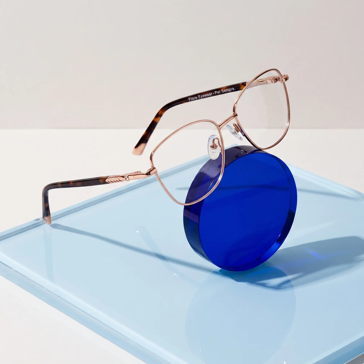 Fiore 2210 eyeglasses in gold pink – on a cobalt acrylic disc in soft daylight