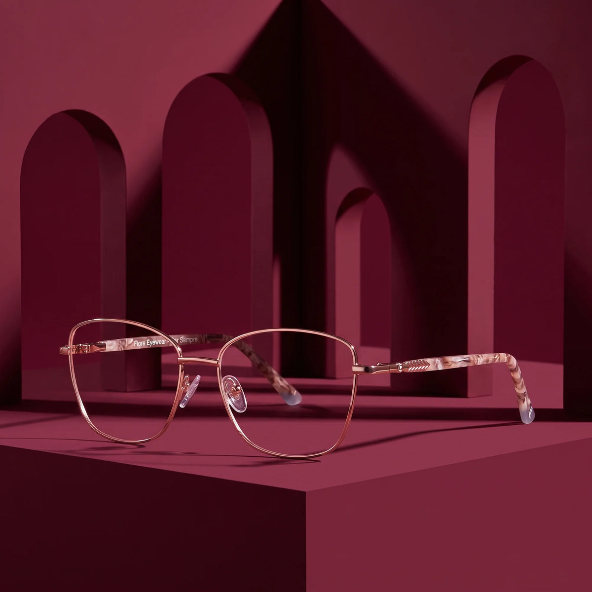 Fiore 2210 eyeglasses in gold brown – displayed on a burgundy podium among arches
