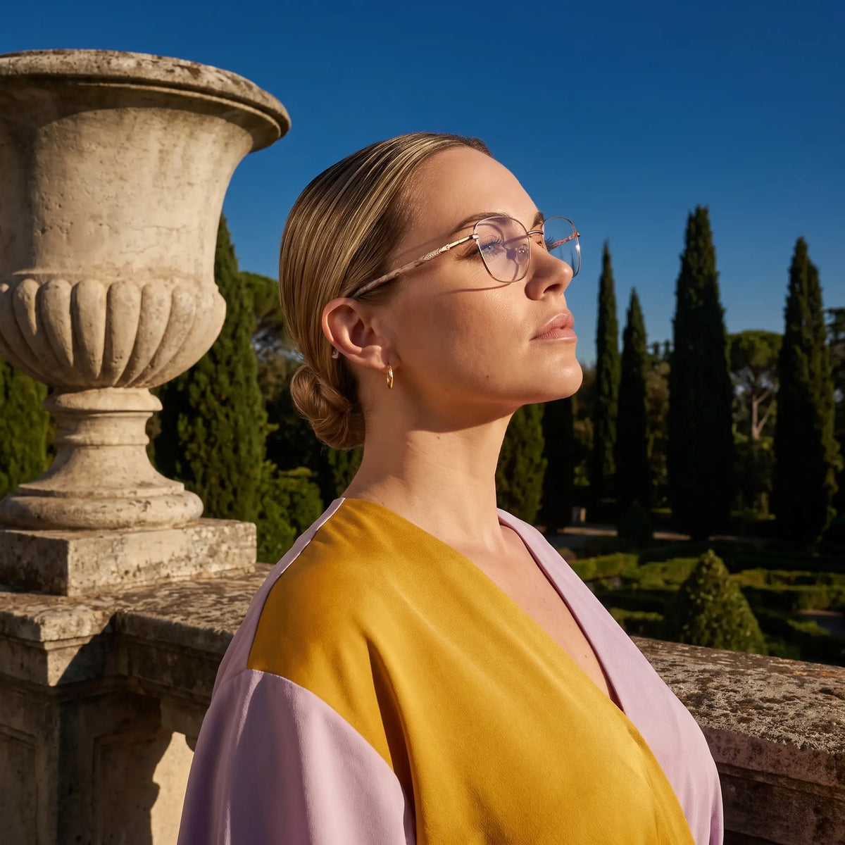 Fiore 2210 eyeglasses in gold brown, worn by a model – campaign portrait, dusk light over a cypress garden