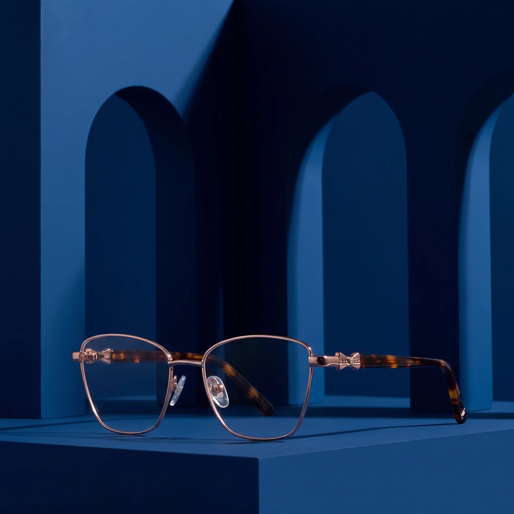 Fiore 22115 eyeglasses in brown – displayed on a midnight blue podium among arches