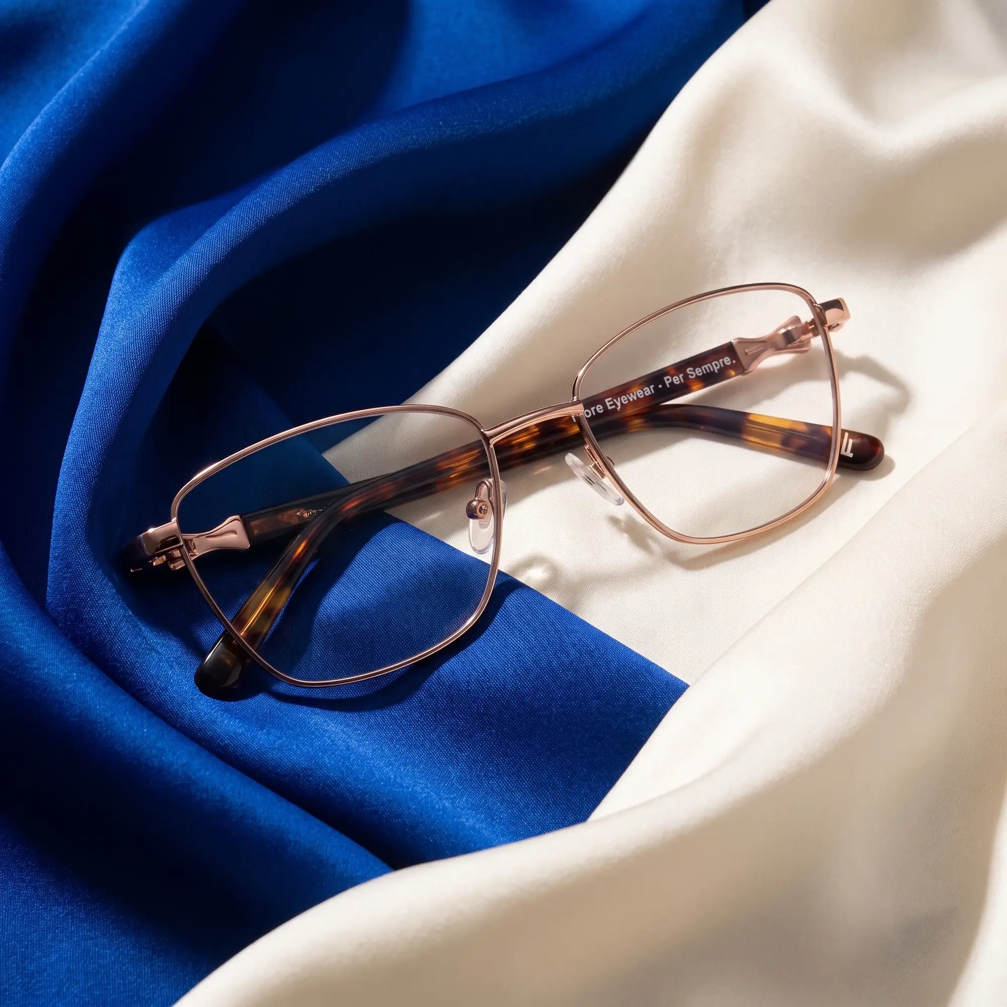 Fiore 22115 eyeglasses in brown – resting on draped cobalt and ivory silk