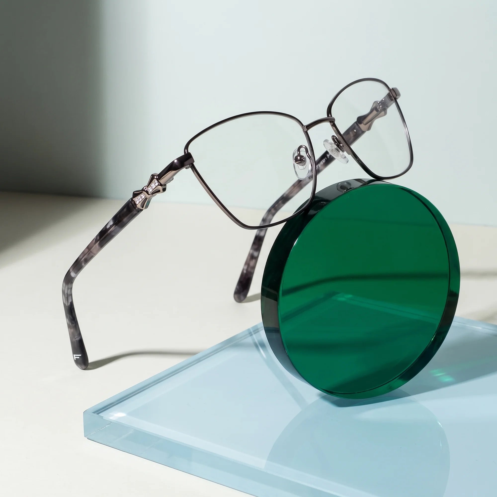 Fiore 22115 eyeglasses in black silver – on a cobalt acrylic disc in soft daylight