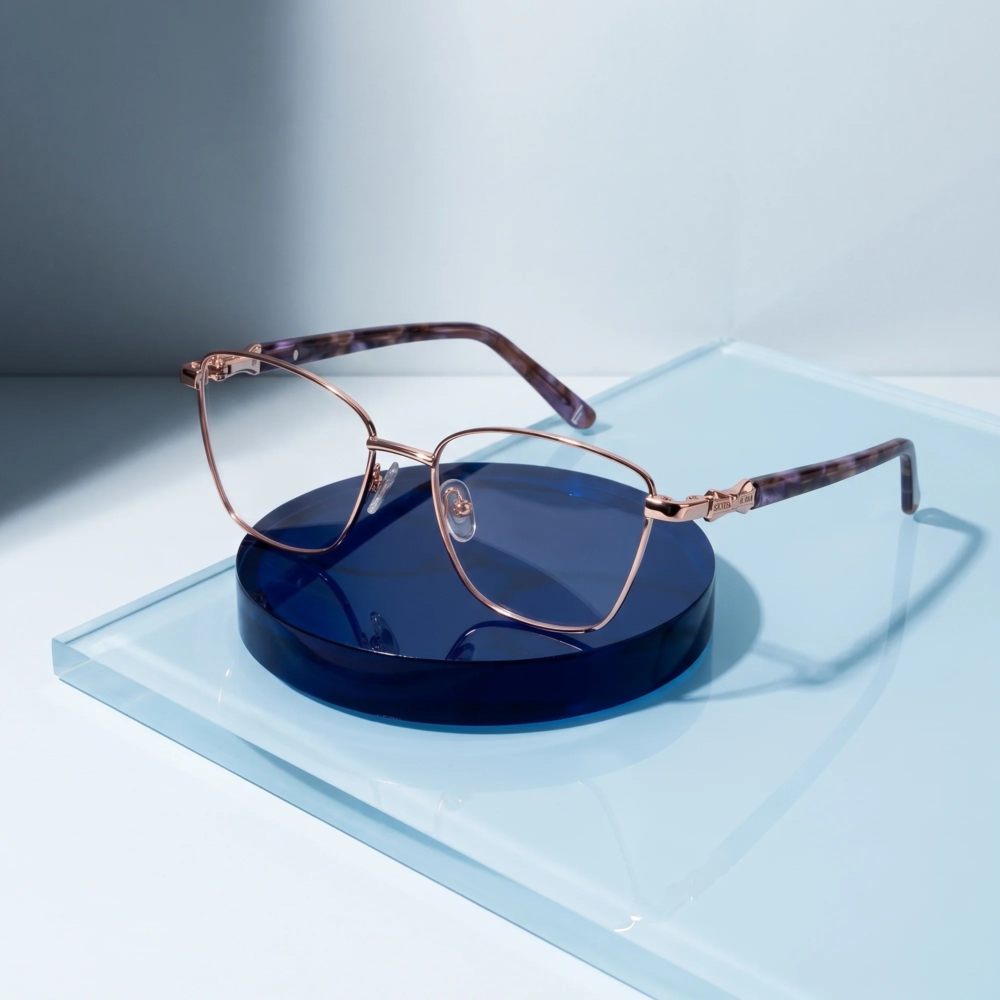 Fiore 22115 eyeglasses in gold – on a cobalt acrylic disc in soft daylight