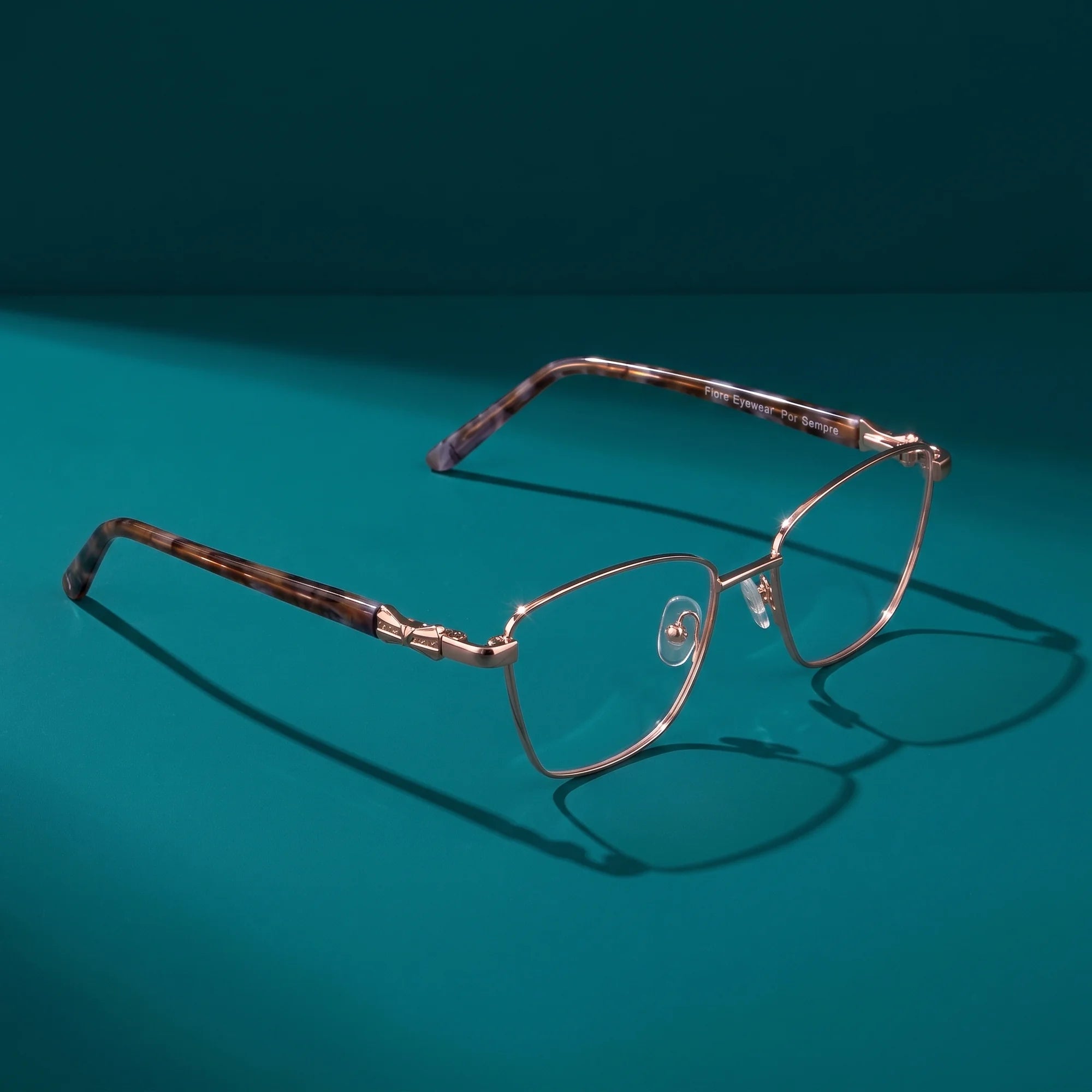 Fiore 22115 eyeglasses in gold – hero still life against a deep teal backdrop