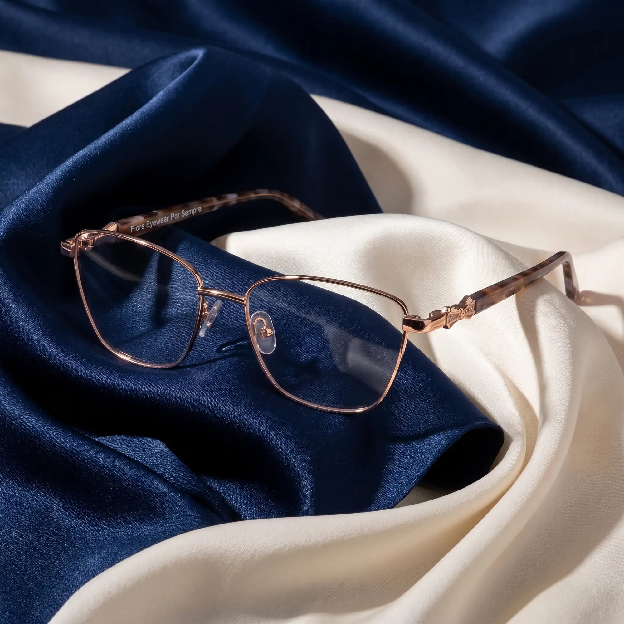 Fiore 22115 eyeglasses in gold – resting on draped midnight blue and ivory silk