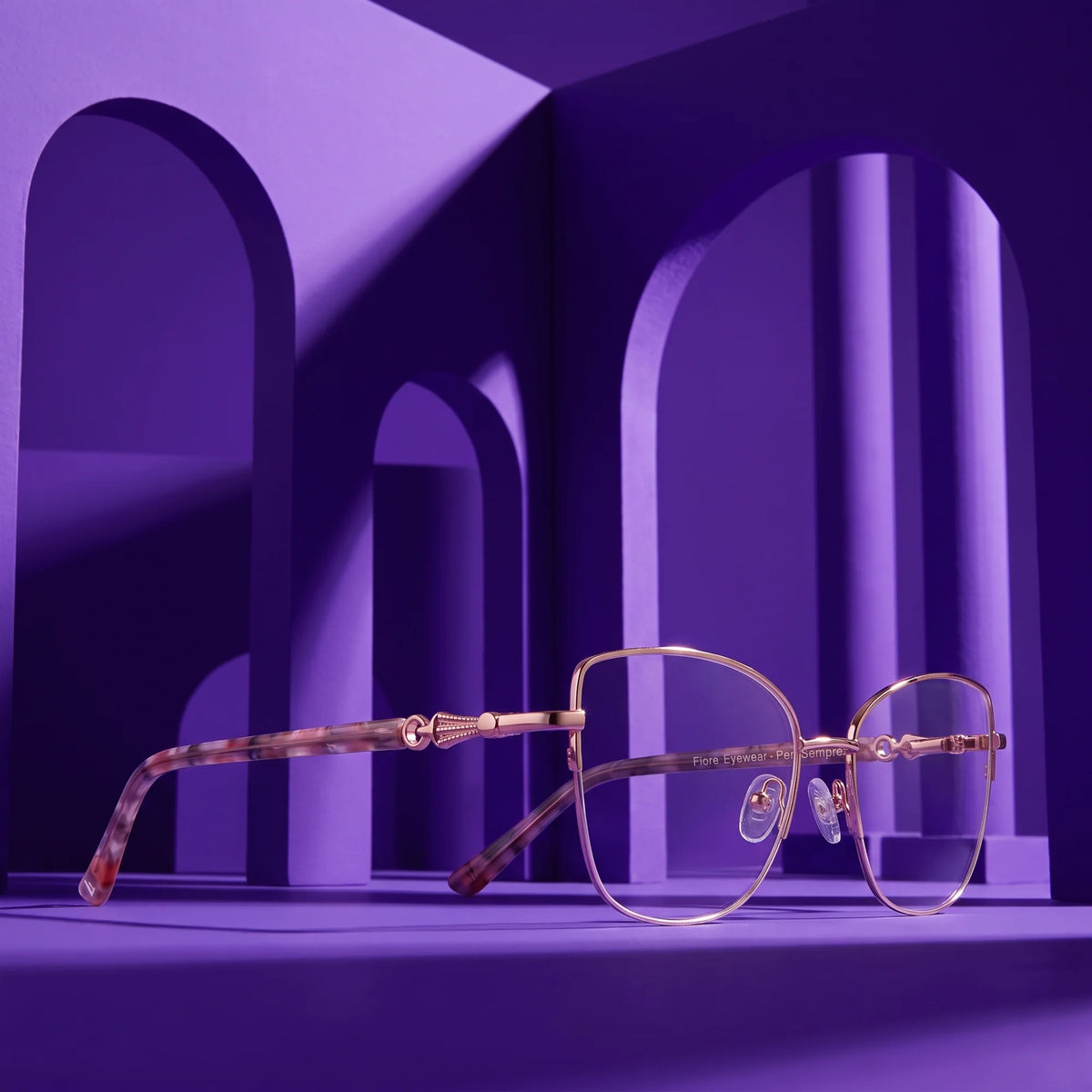 Fiore 22117 eyeglasses in gold – displayed on a saturated color podium among arches