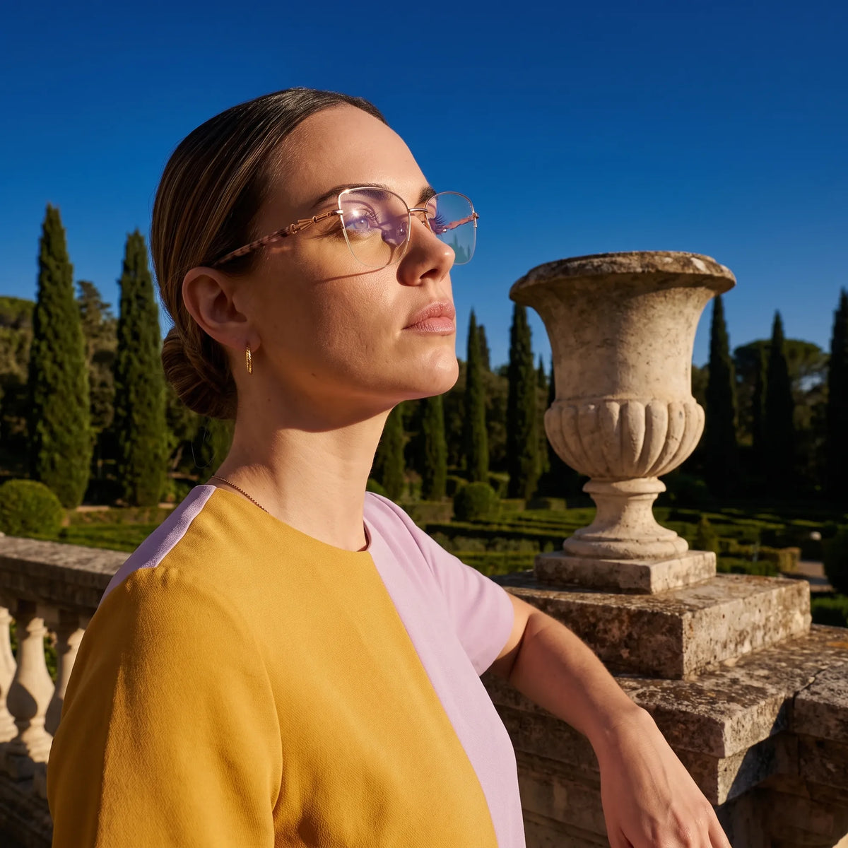 Fiore 22117 eyeglasses in gold, worn by a model – campaign portrait, dusk light over a cypress garden