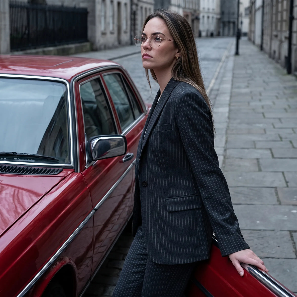 Fiore 22117 eyeglasses in gold, worn by a model – campaign portrait, pinstripe suit beside a classic red car