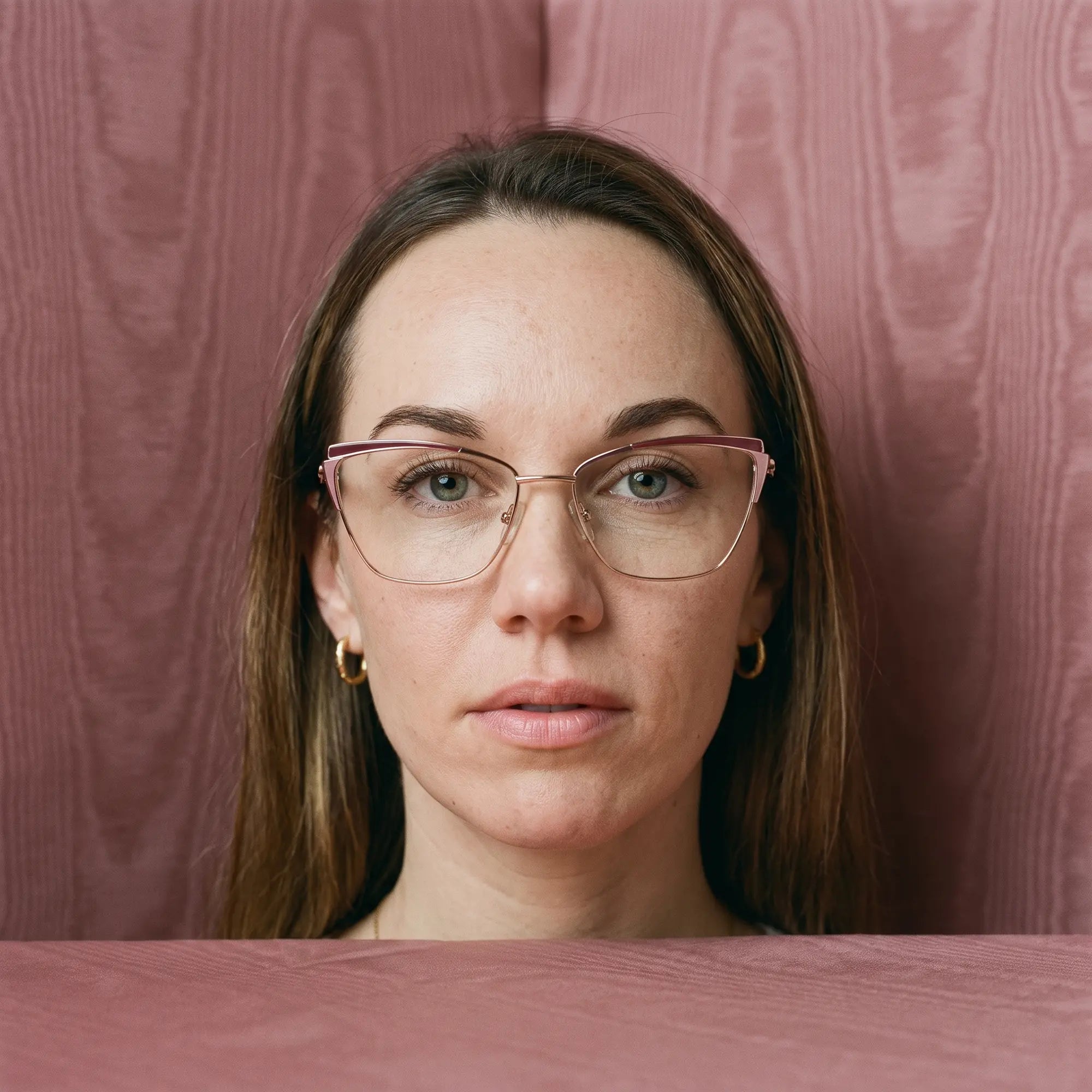 Fiore 3837 eyeglasses in red gold, worn by a model – campaign portrait, face framed by rose moire upholstery