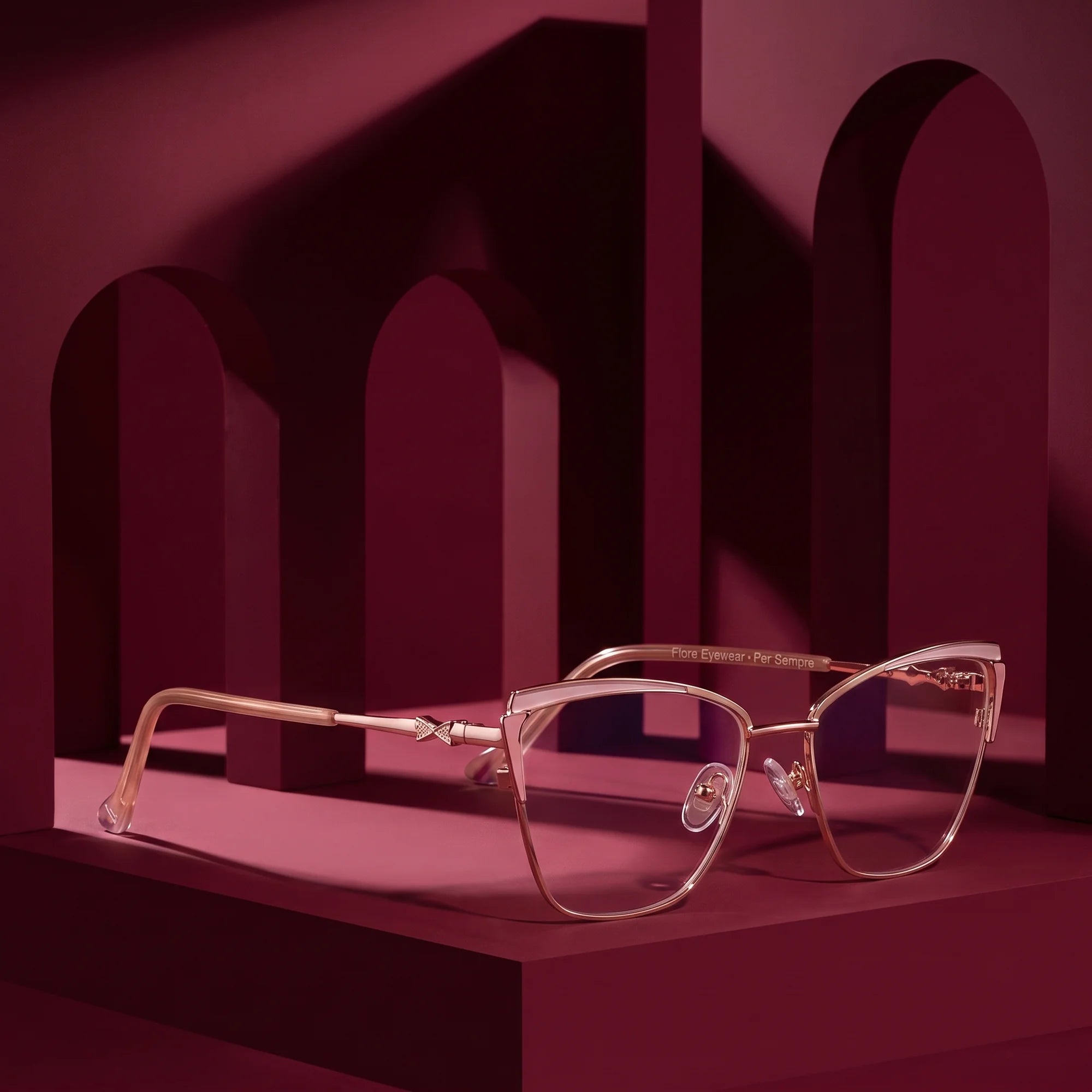 Fiore 3837 eyeglasses in pink gold – displayed on a burgundy podium among arches