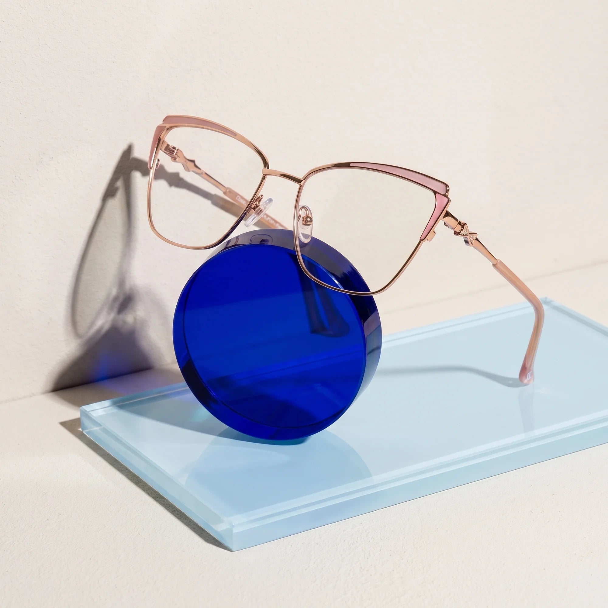 Fiore 3837 eyeglasses in pink gold – on a cobalt acrylic disc in soft daylight