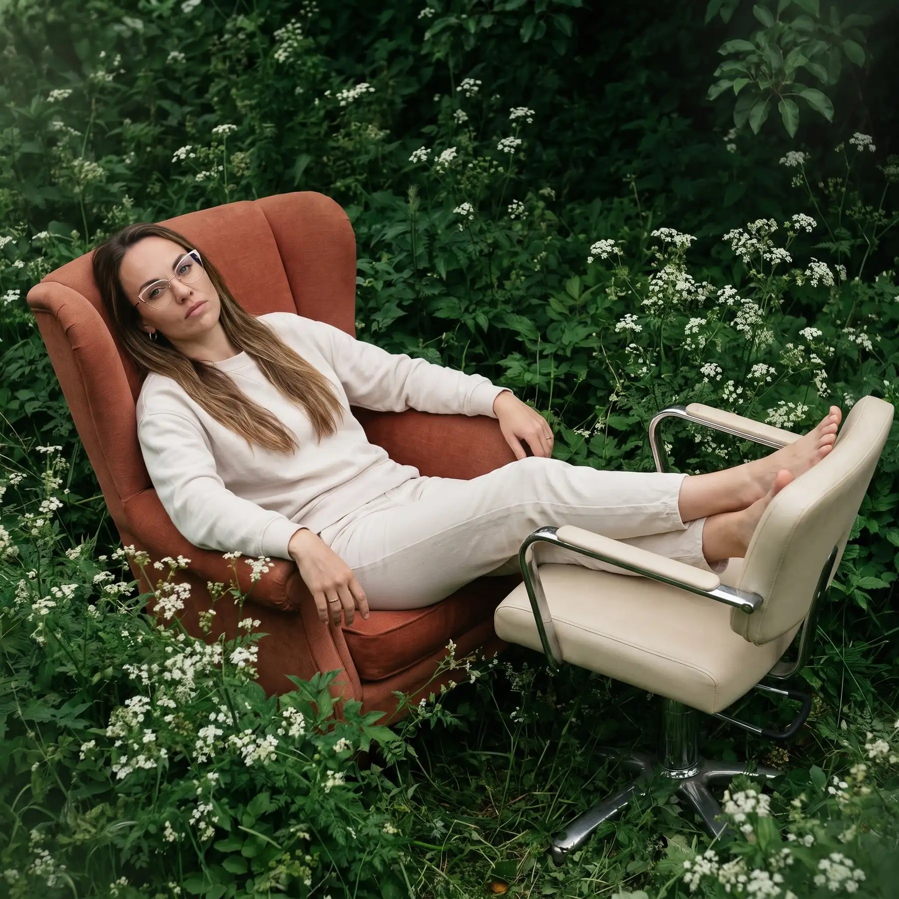 Fiore 3837 eyeglasses in pink gold, worn by a model – campaign portrait, lounging in an armchair in a wildflower meadow