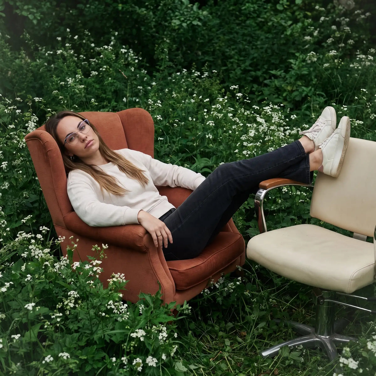 Fiore 3839 eyeglasses in purple silver, worn by a model – campaign portrait, lounging in an armchair in a wildflower meadow