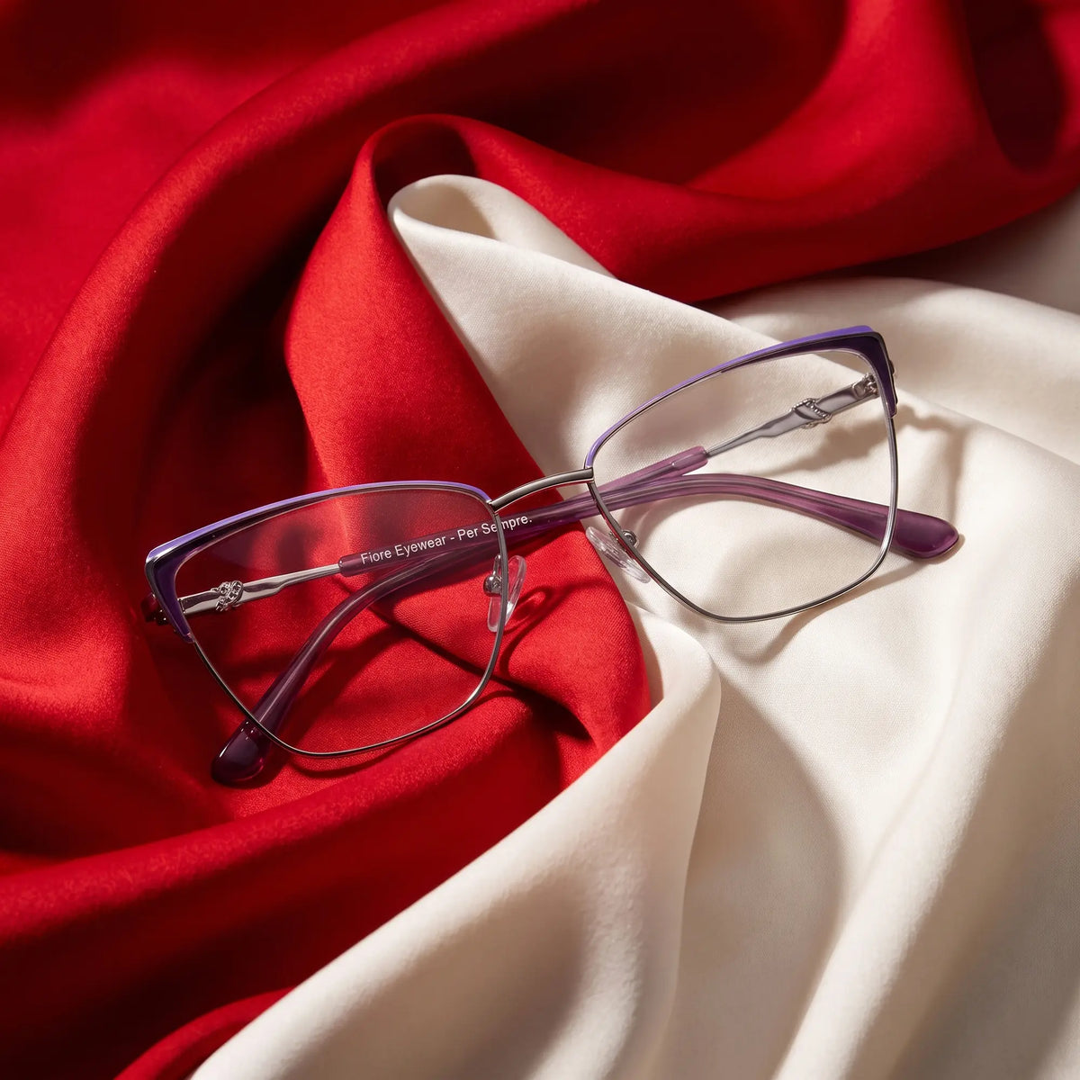Fiore 3839 eyeglasses in purple silver – resting on draped vivid red and ivory silk