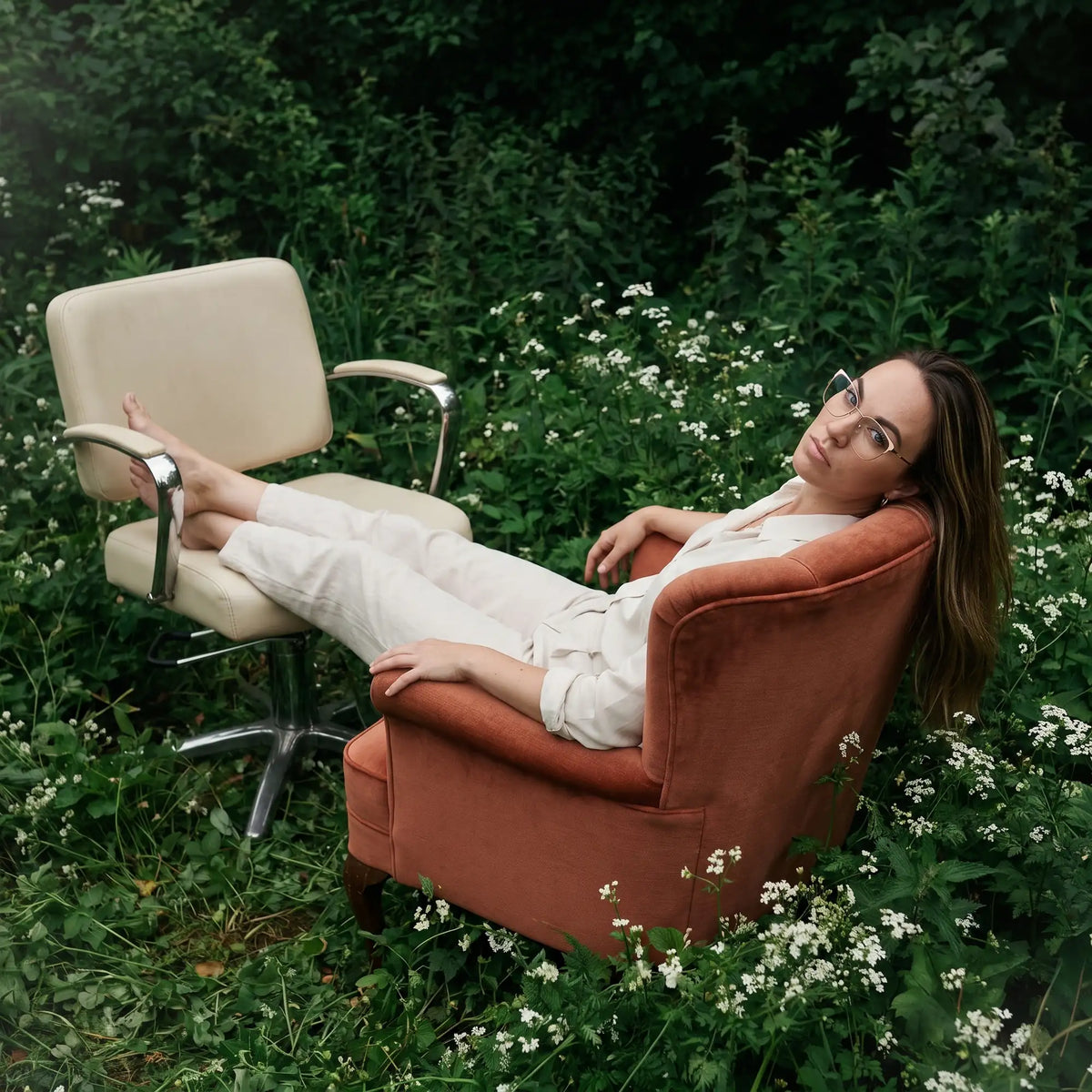 Fiore 3839 eyeglasses in pink gold, worn by a model – campaign portrait, lounging in an armchair in a wildflower meadow