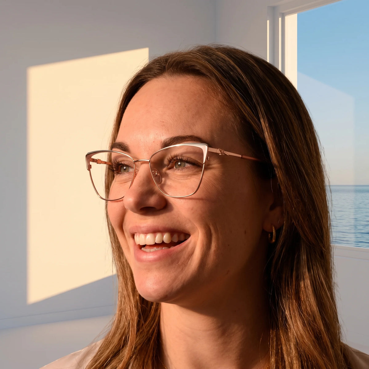 Fiore 3839 eyeglasses in pink gold, worn by a model – campaign portrait, smiling at a bright window over the sea