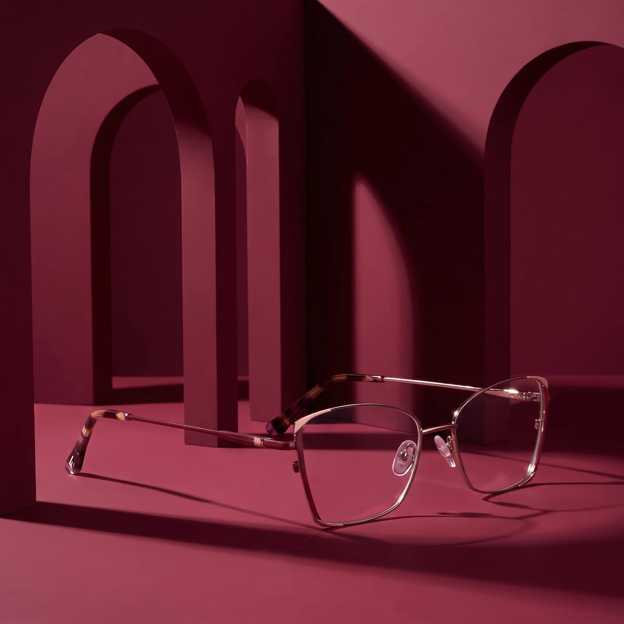Fiore 3916 eyeglasses in purple pink silver – displayed on a burgundy podium among arches