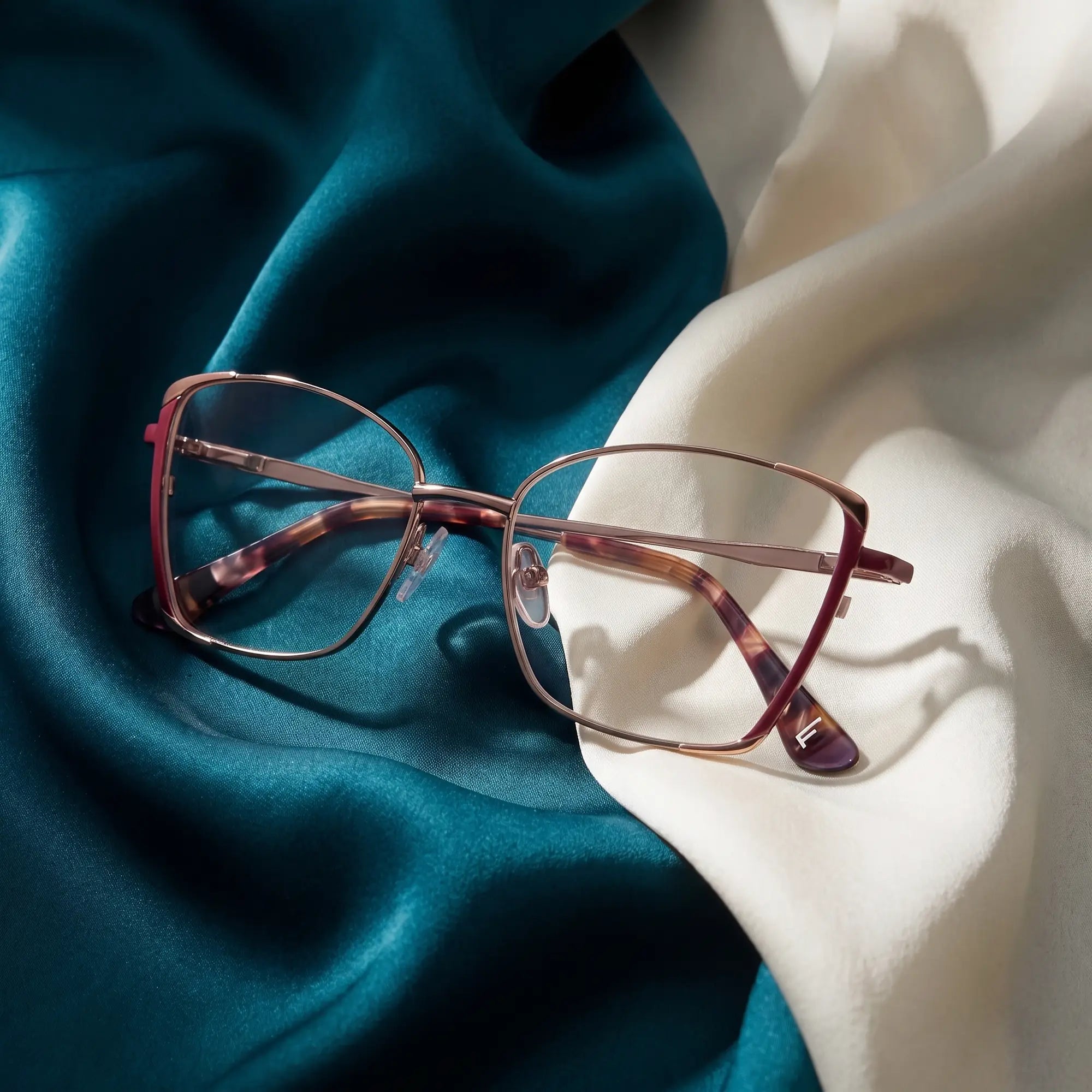 Fiore 3916 eyeglasses in purple pink silver – resting on draped teal and ivory silk