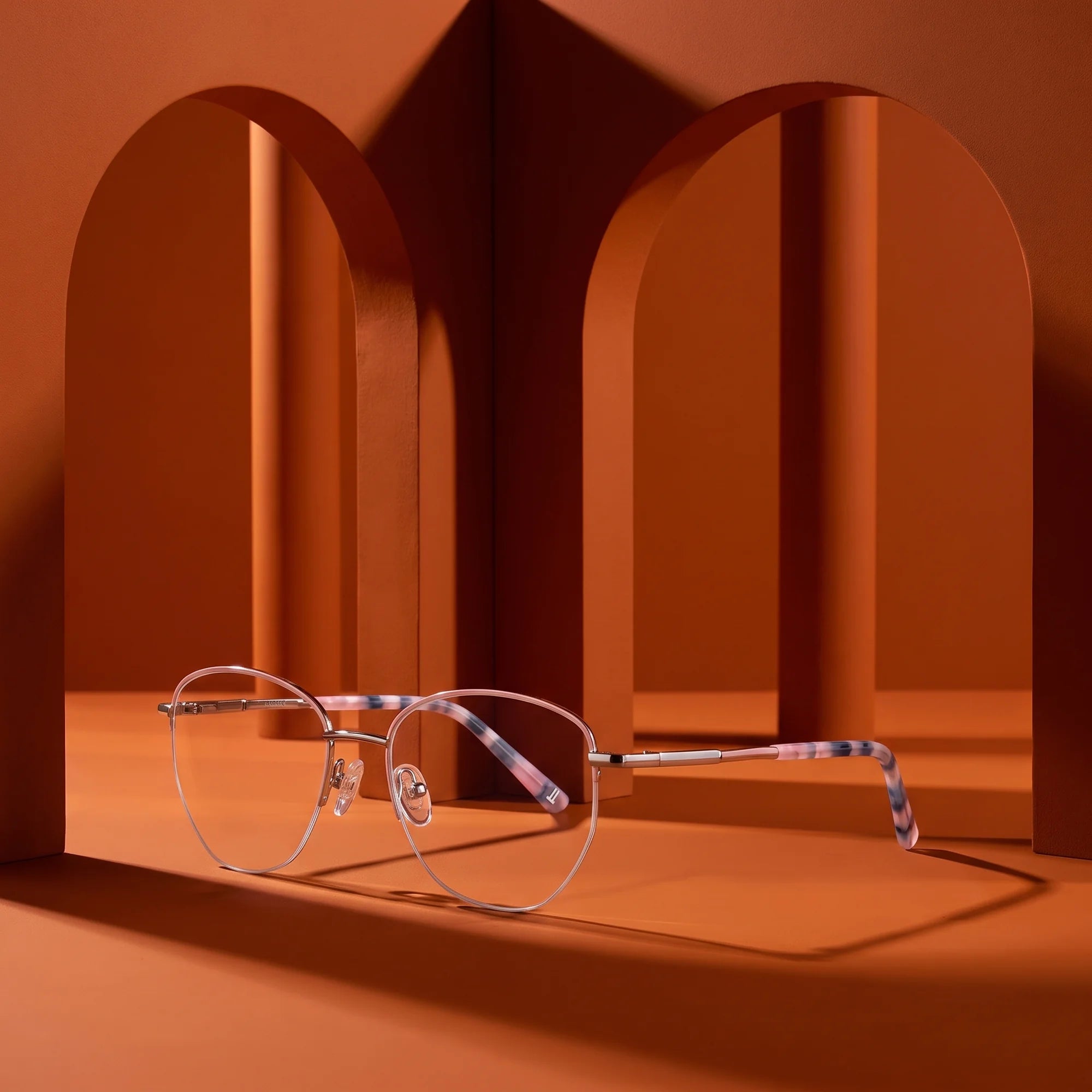 Fiore 3921 eyeglasses in pink silver – displayed on a burnt orange podium among arches
