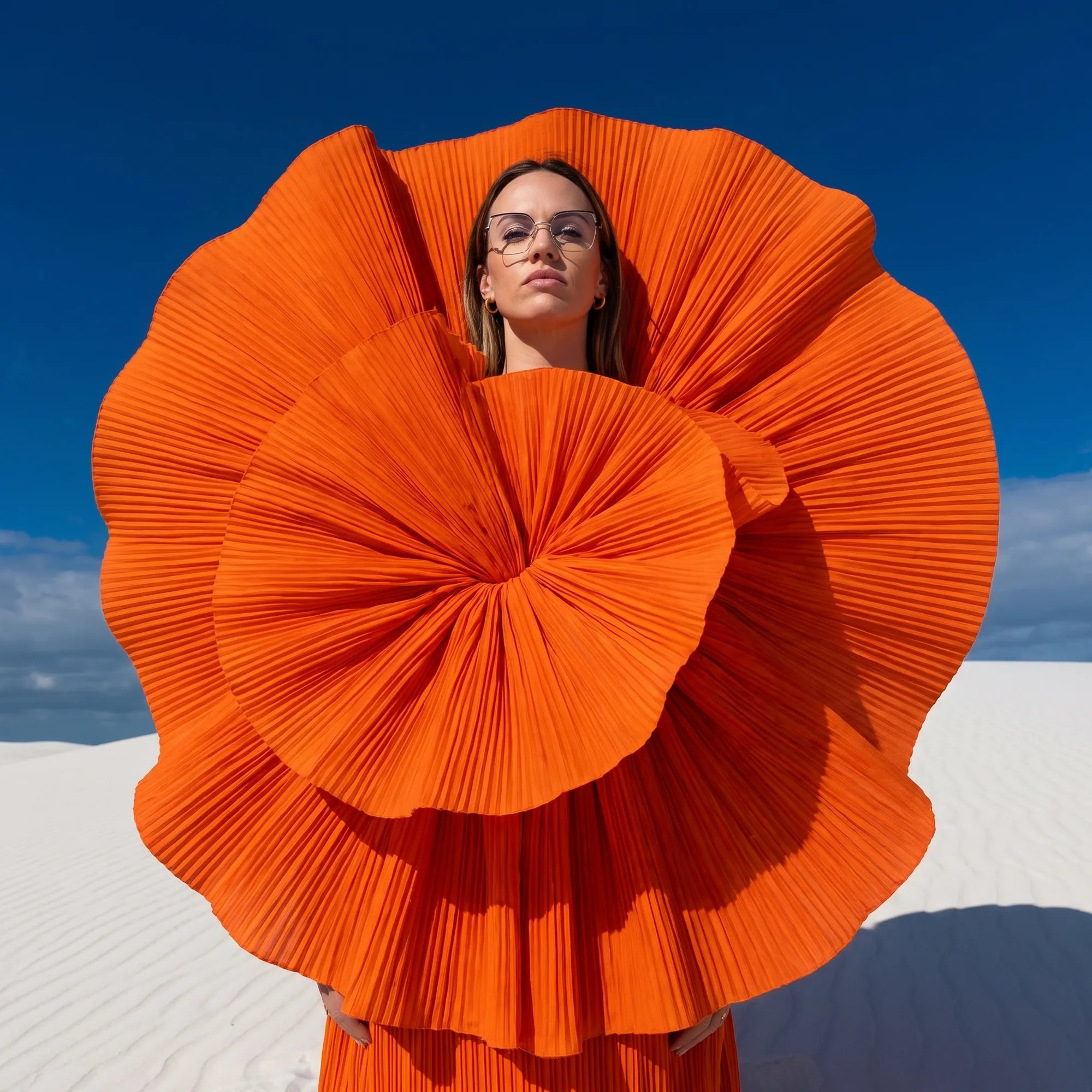 Fiore 3971 eyeglasses in black gold, worn by a model – campaign portrait, sculptural orange pleated fan on white dunes