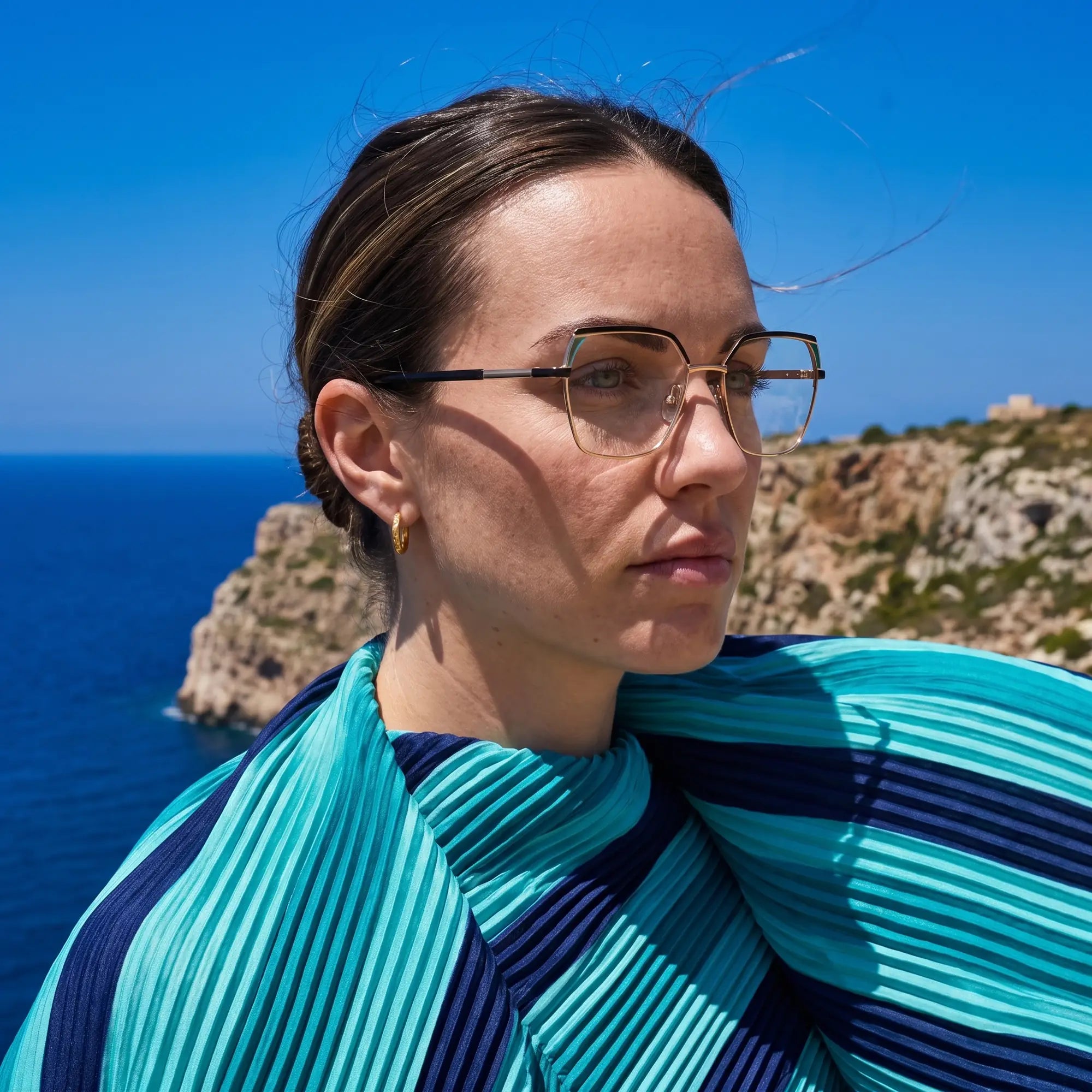 Fiore 3971 eyeglasses in black gold, worn by a model – campaign portrait, windswept portrait over the deep blue sea