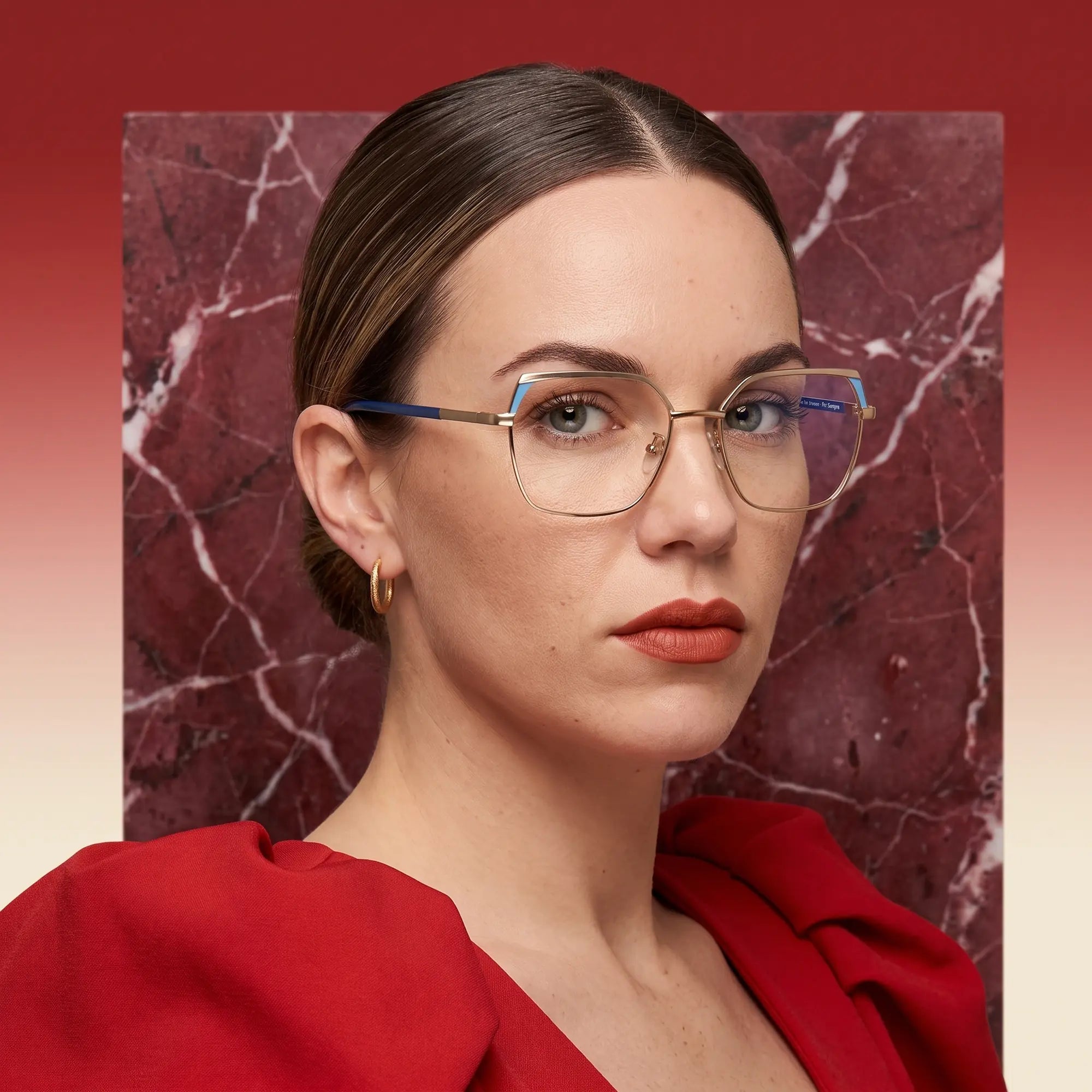 Fiore 3971 eyeglasses in grey gold, worn by a model – campaign portrait, red marble backdrop and draped scarlet dress