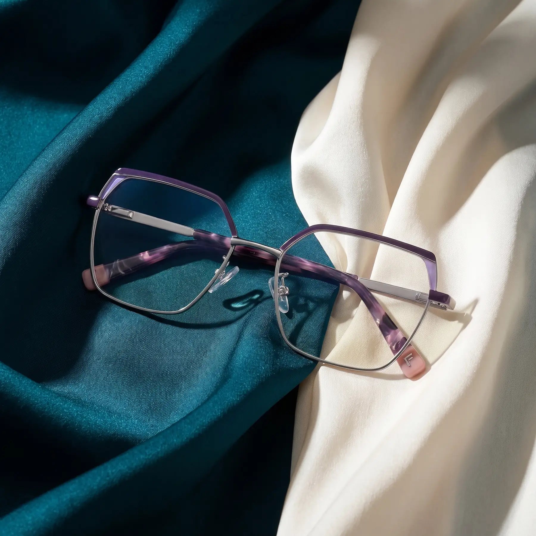 Fiore 3971 eyeglasses in purple silver – resting on draped teal and ivory silk