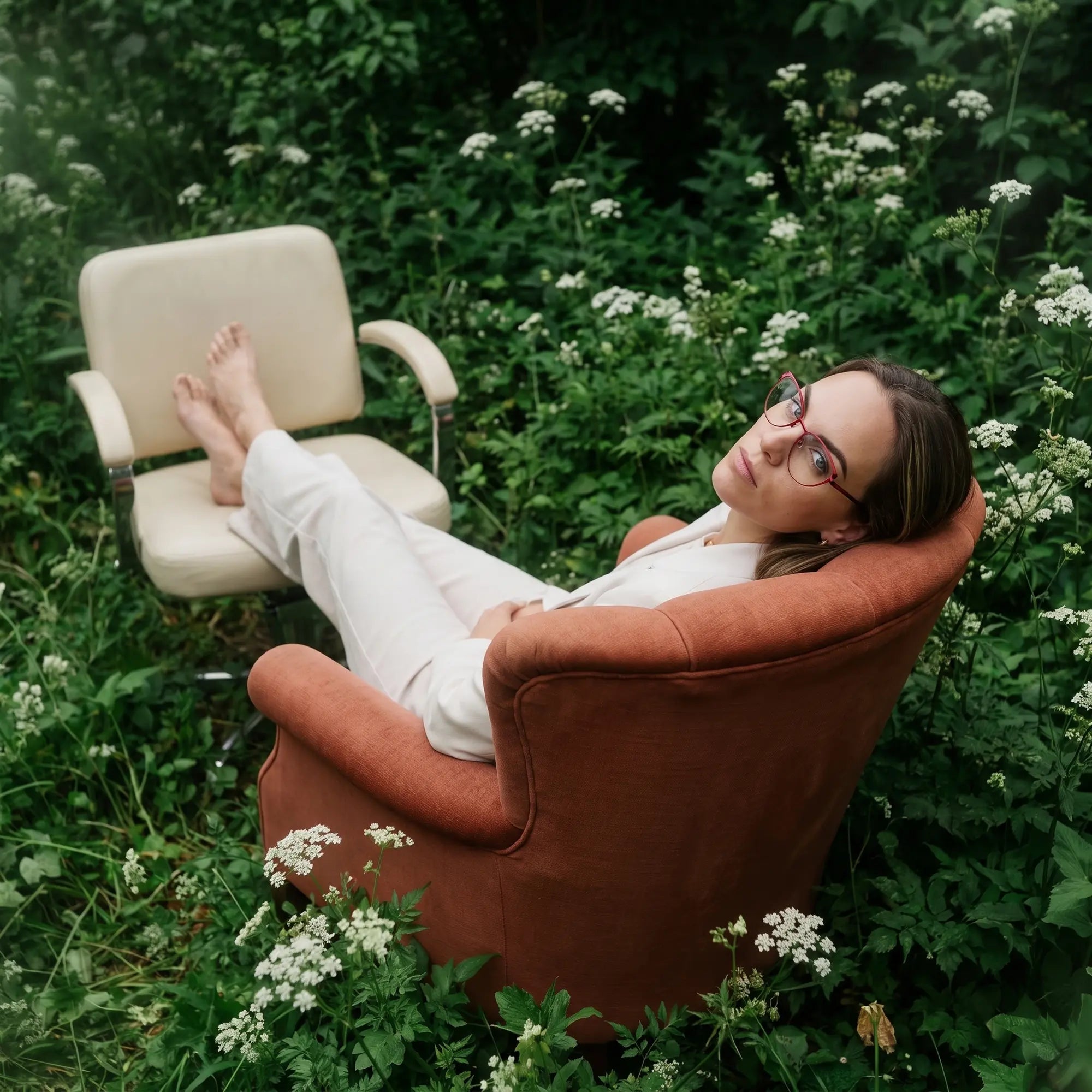 Fiore 3983 eyeglasses in red black, worn by a model – campaign portrait, lounging in an armchair in a wildflower meadow