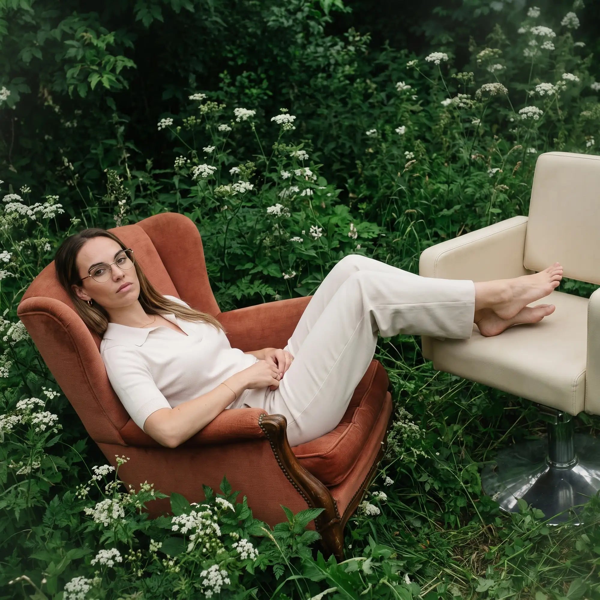 Fiore 3983 eyeglasses in brown gold, worn by a model – campaign portrait, lounging in an armchair in a wildflower meadow