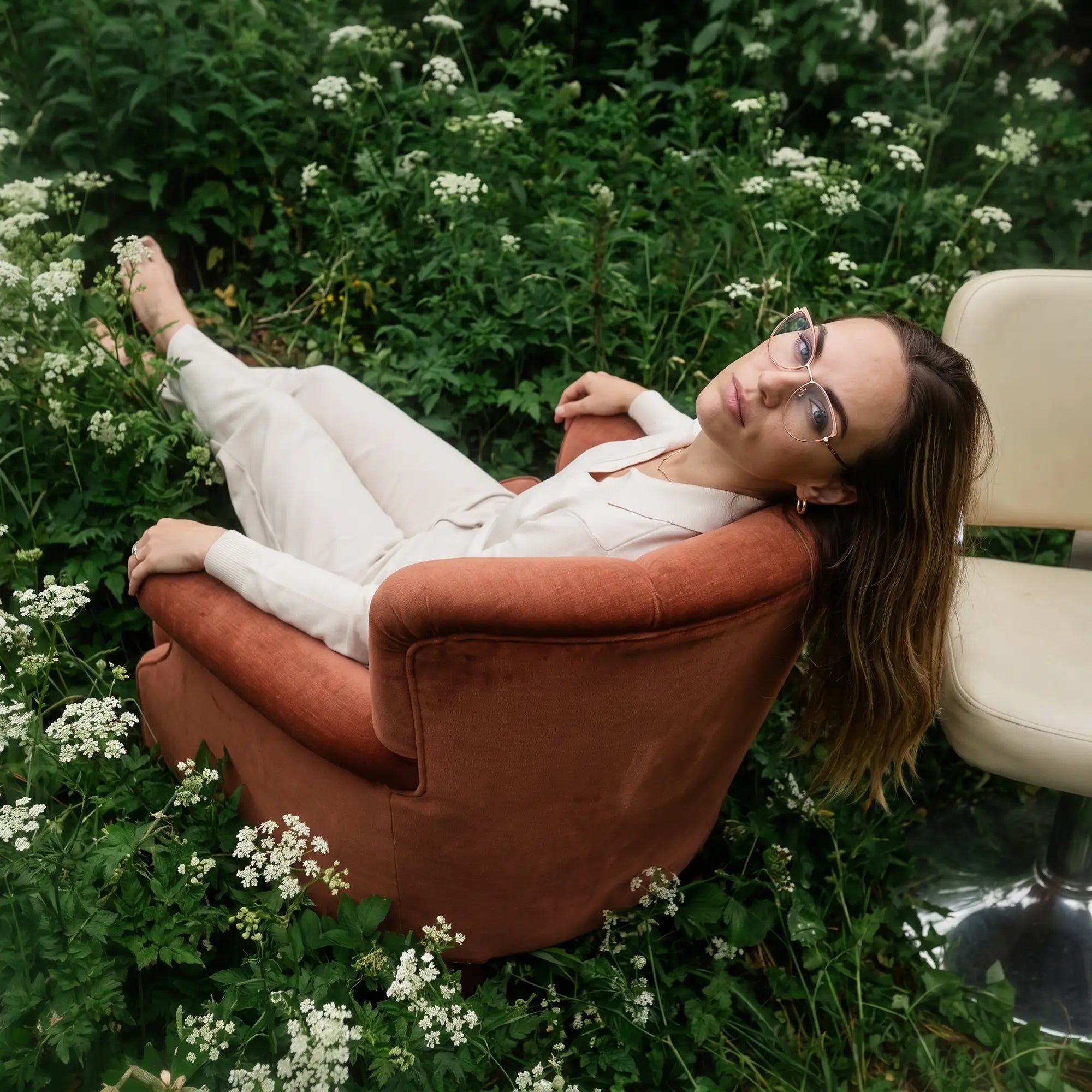 Fiore 3983 eyeglasses in pink gold, worn by a model – campaign portrait, lounging in an armchair in a wildflower meadow