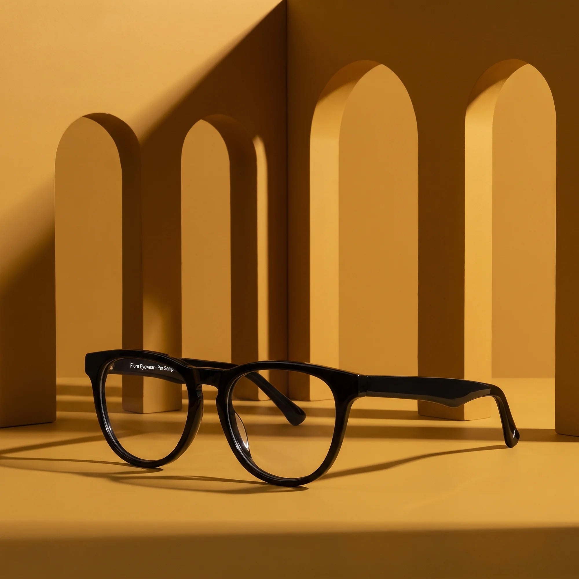 Fiore 4488 eyeglasses in black – displayed on a mustard ochre podium among arches