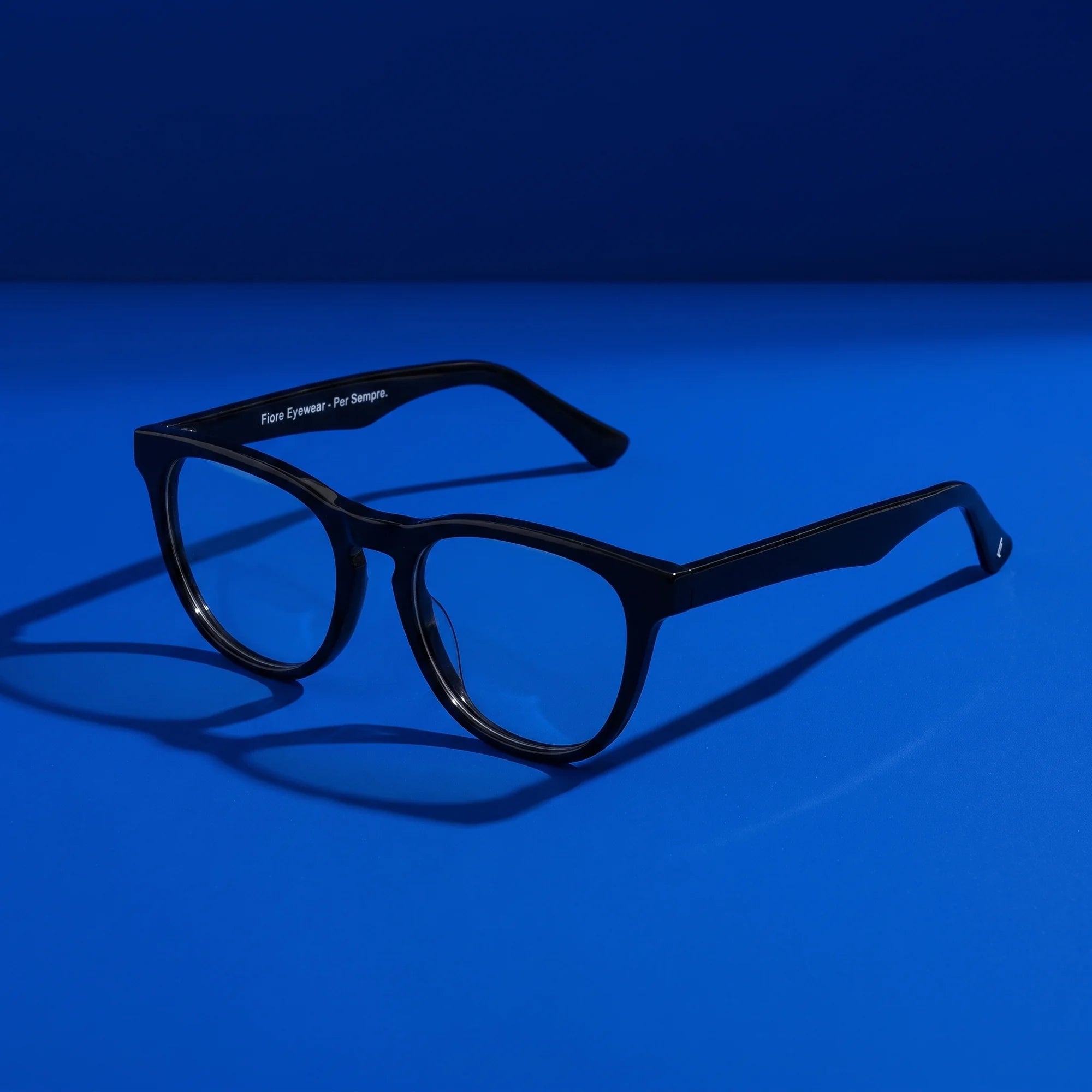 Fiore 4488 eyeglasses in black – hero still life against a deep cobalt backdrop