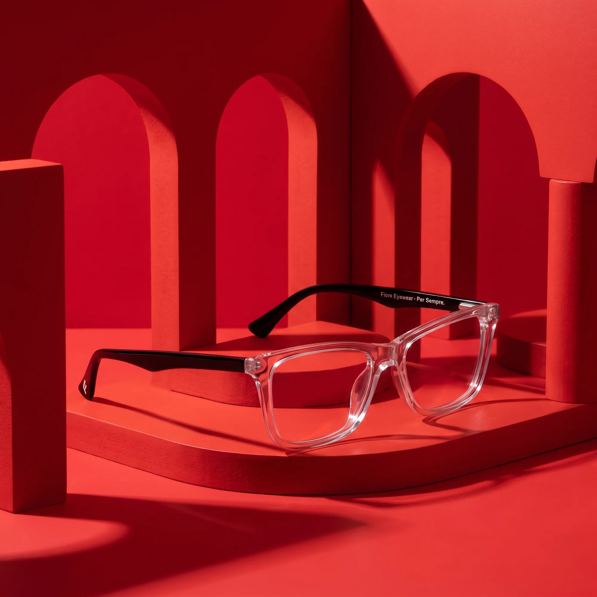 Fiore 5228 eyeglasses in transparent – displayed on a vivid red podium among arches