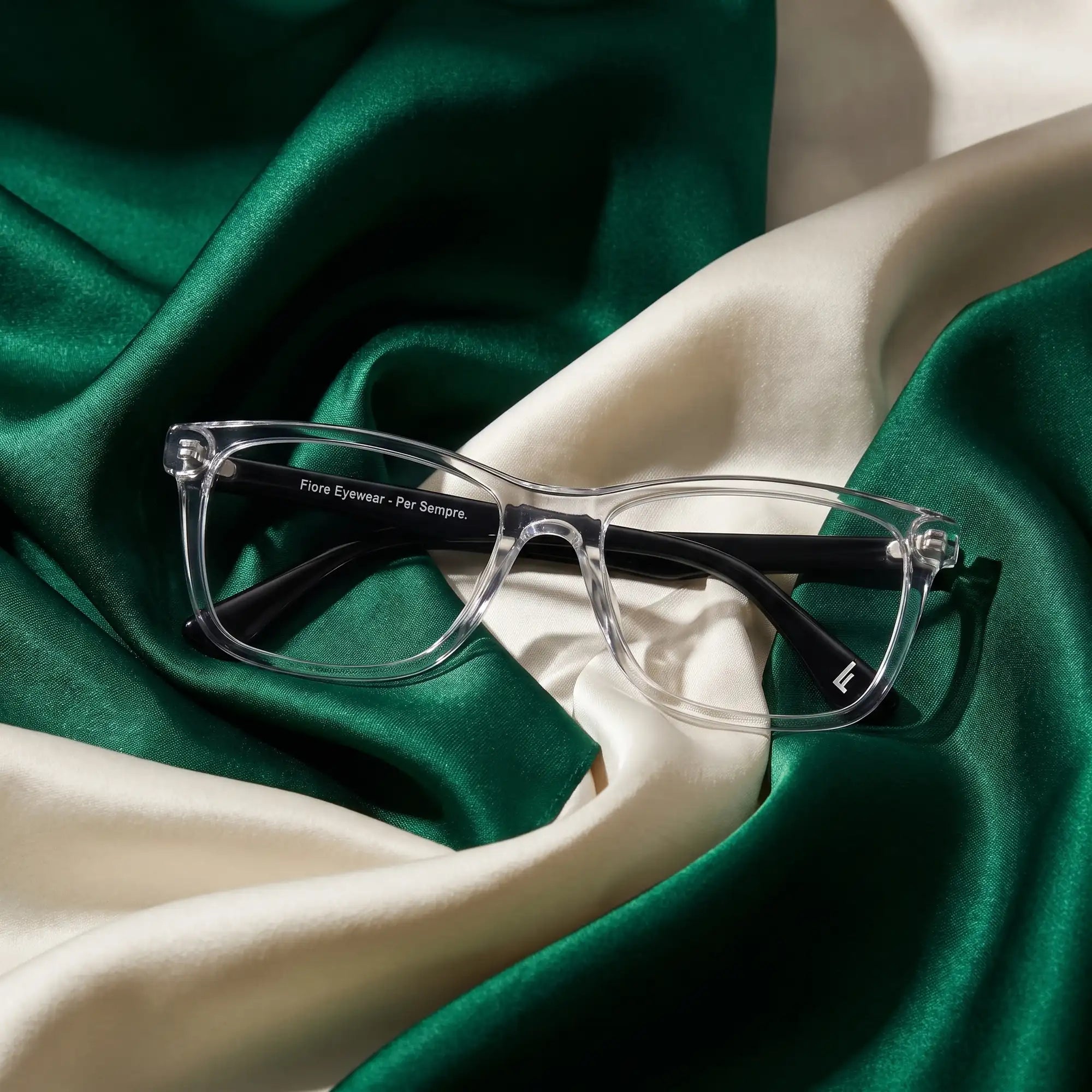 Fiore 5228 eyeglasses in transparent – resting on draped emerald and ivory silk