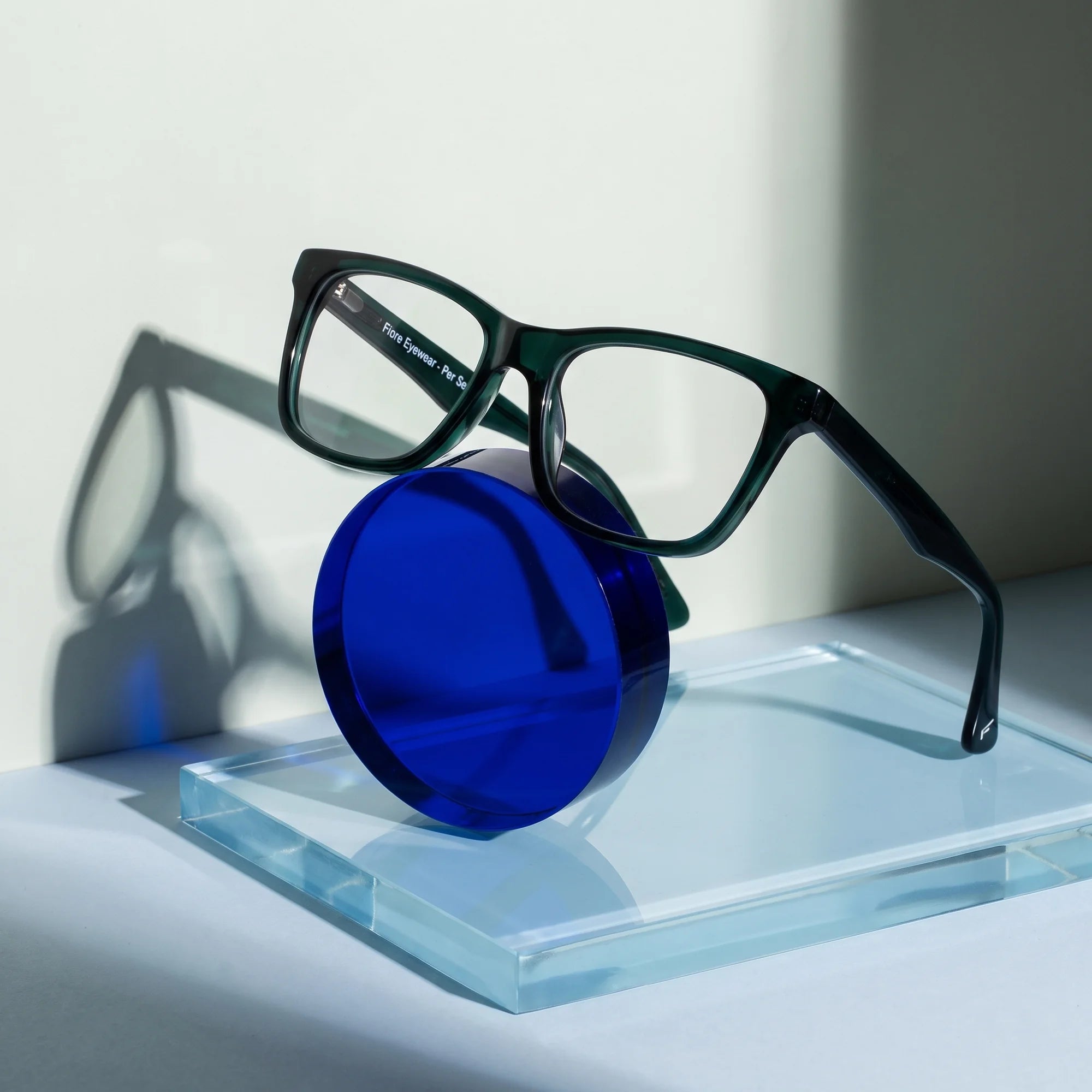 Fiore 5228 eyeglasses in green – on a cobalt acrylic disc in soft daylight