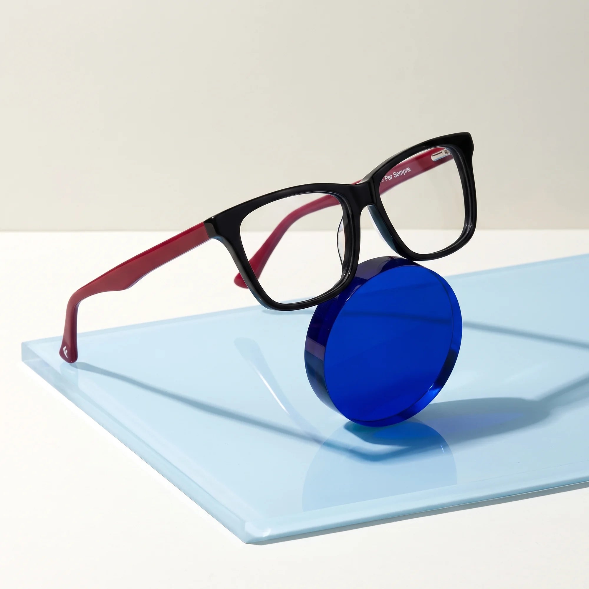 Fiore 5228 eyeglasses in black – on a cobalt acrylic disc in soft daylight