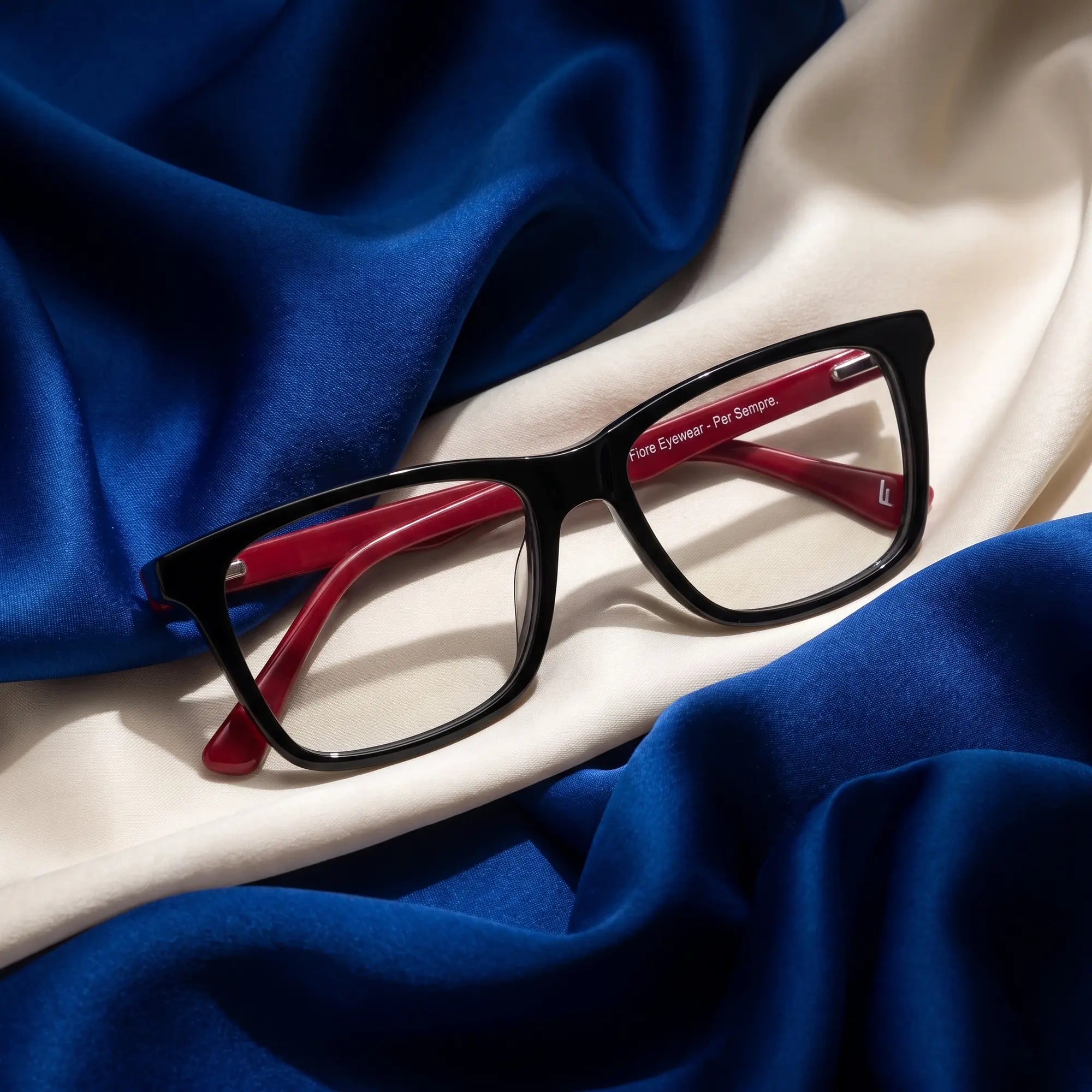 Fiore 5228 eyeglasses in black – resting on draped cobalt and ivory silk