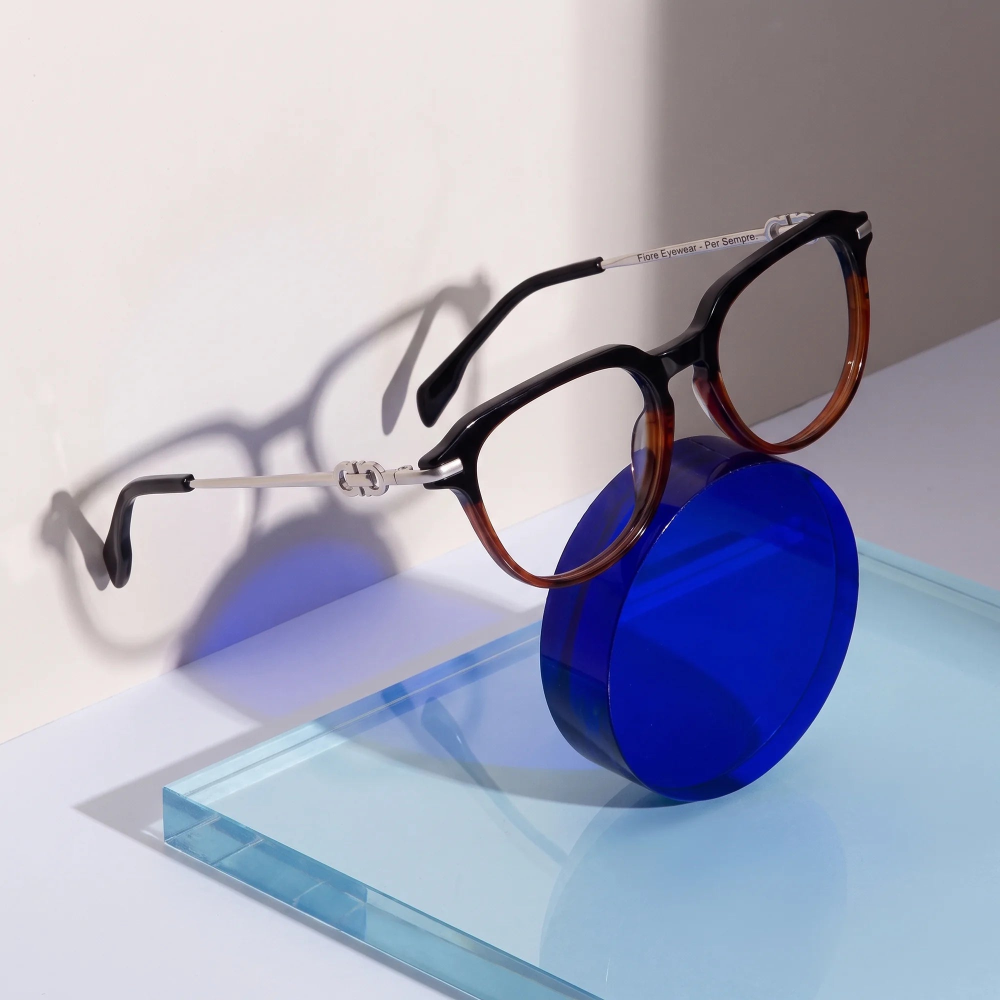 Fiore 5409 eyeglasses in black brown – on a cobalt acrylic disc in soft daylight