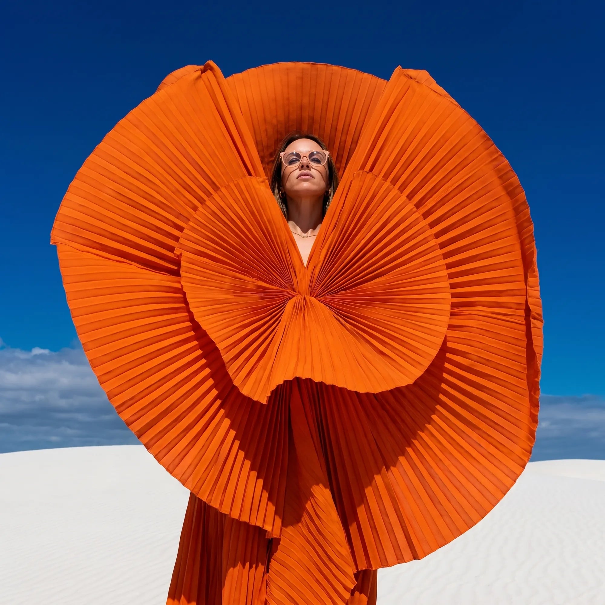 Fiore 5409 eyeglasses in milky white, worn by a model – campaign portrait, sculptural orange pleated fan on white dunes
