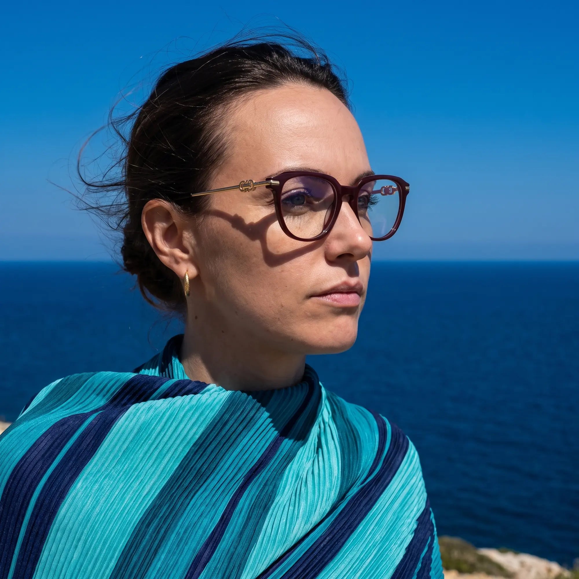 Fiore 5409 eyeglasses in brown red, worn by a model – campaign portrait, windswept portrait over the deep blue sea