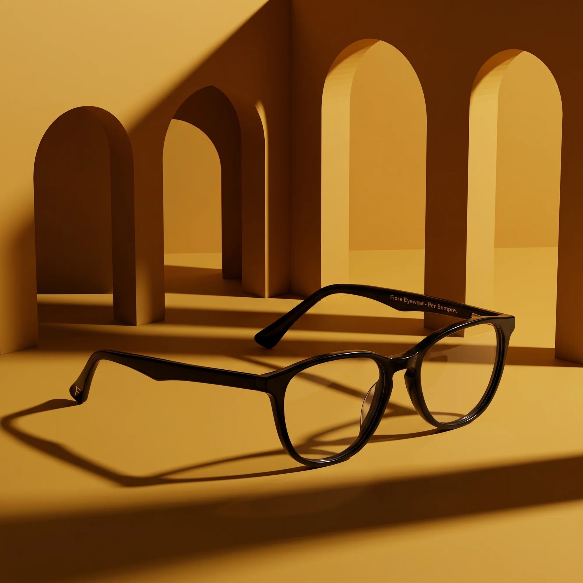 Fiore 7046 eyeglasses in black – displayed on a mustard ochre podium among arches
